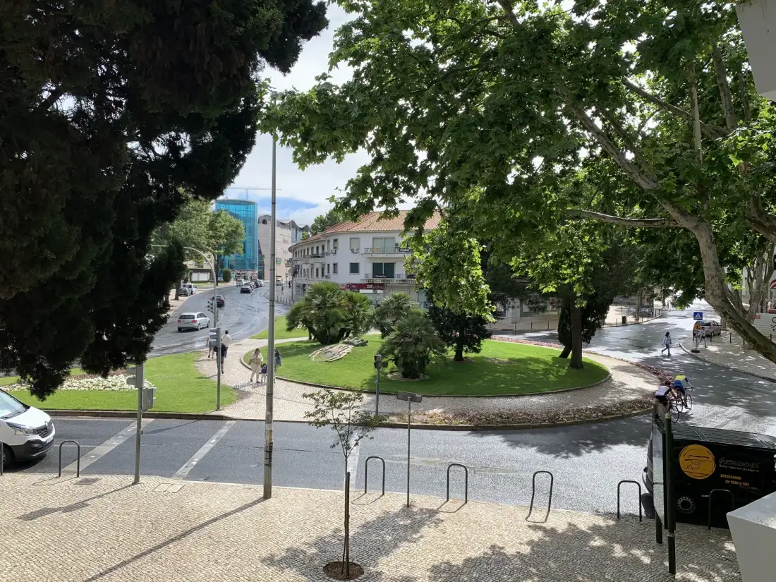 Una rotonda arbolada rodea un pequeño parque verde con senderos y bancos.