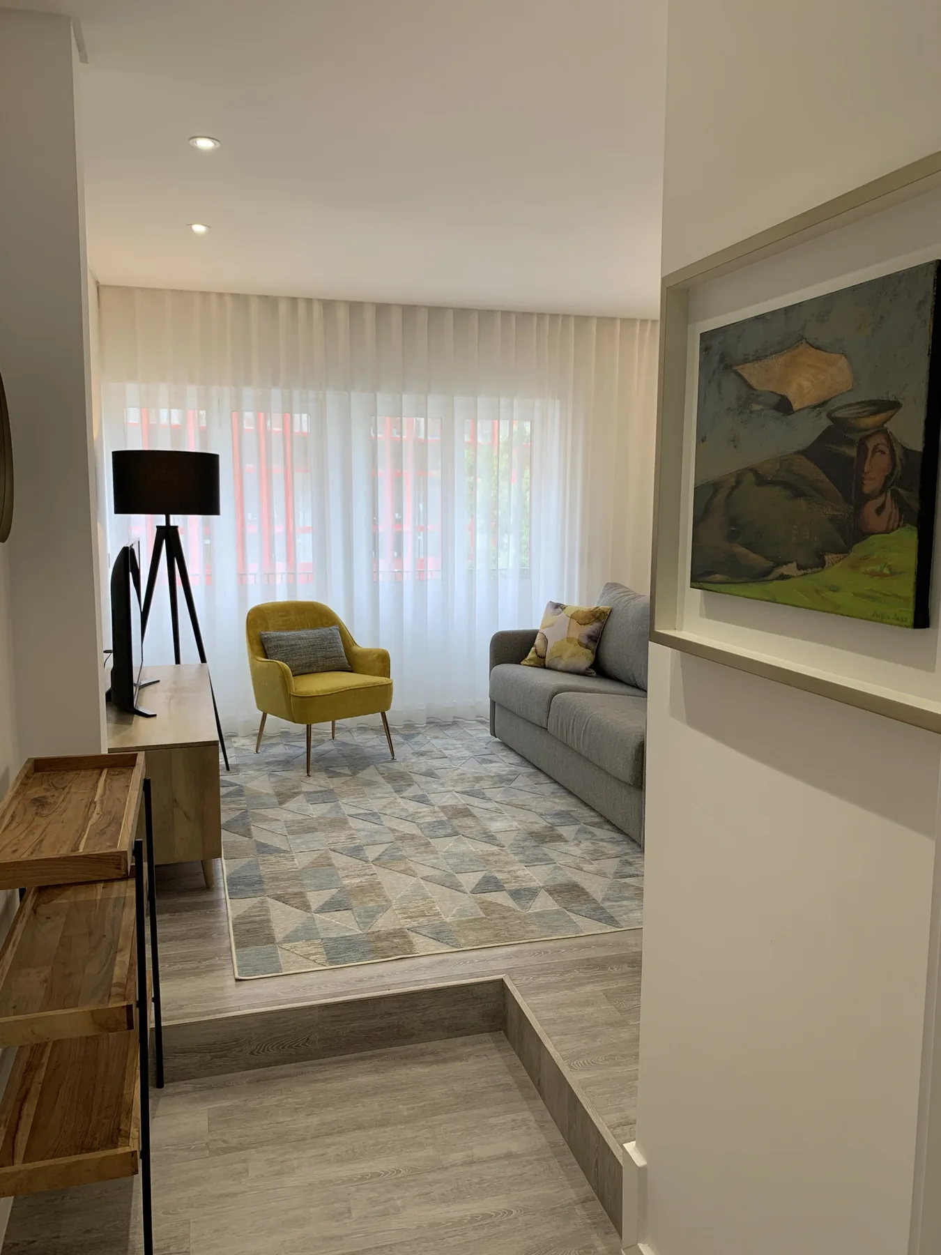 Una sala de estar con asientos, una alfombra y cortinas translúcidas frente a la ventana.