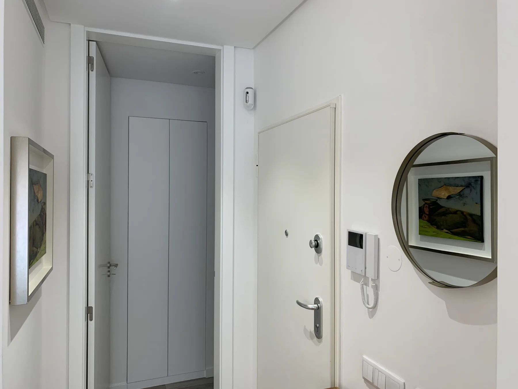 Entrada de un apartamento con una puerta, un interfono y un espejo redondo.