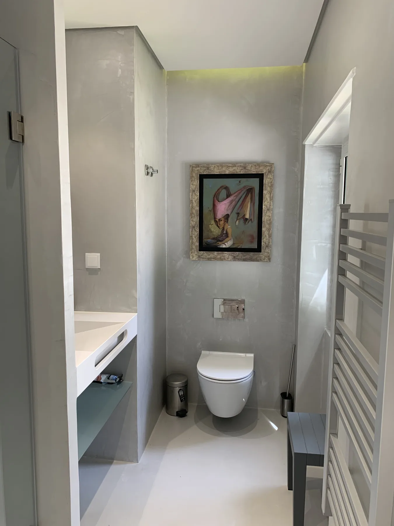 Un baño moderno con un inodoro suspendido y una obra enmarcada.