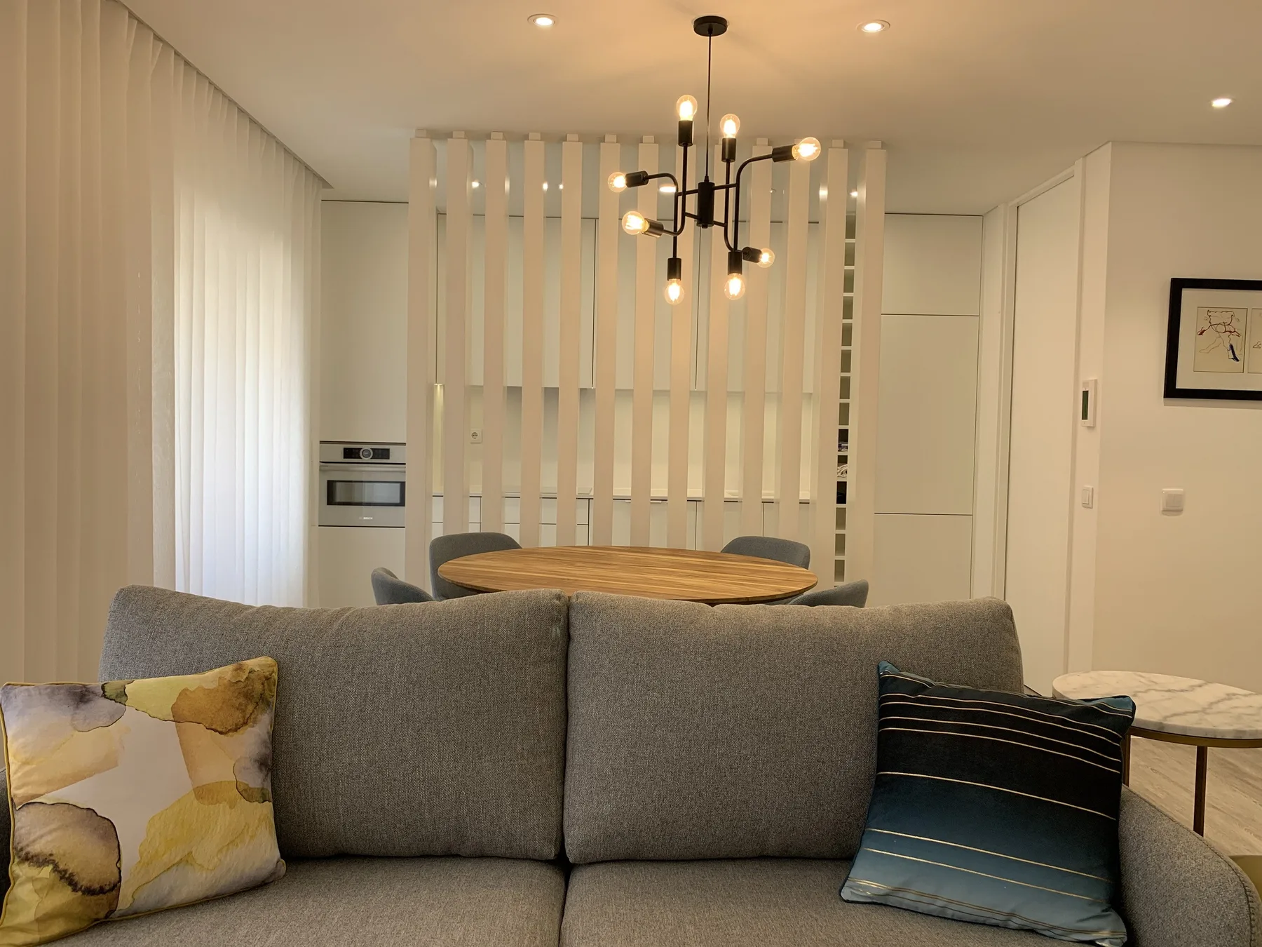Sala de estar y comedor con asientos grises y una mesa detrás de un separador de listones.
