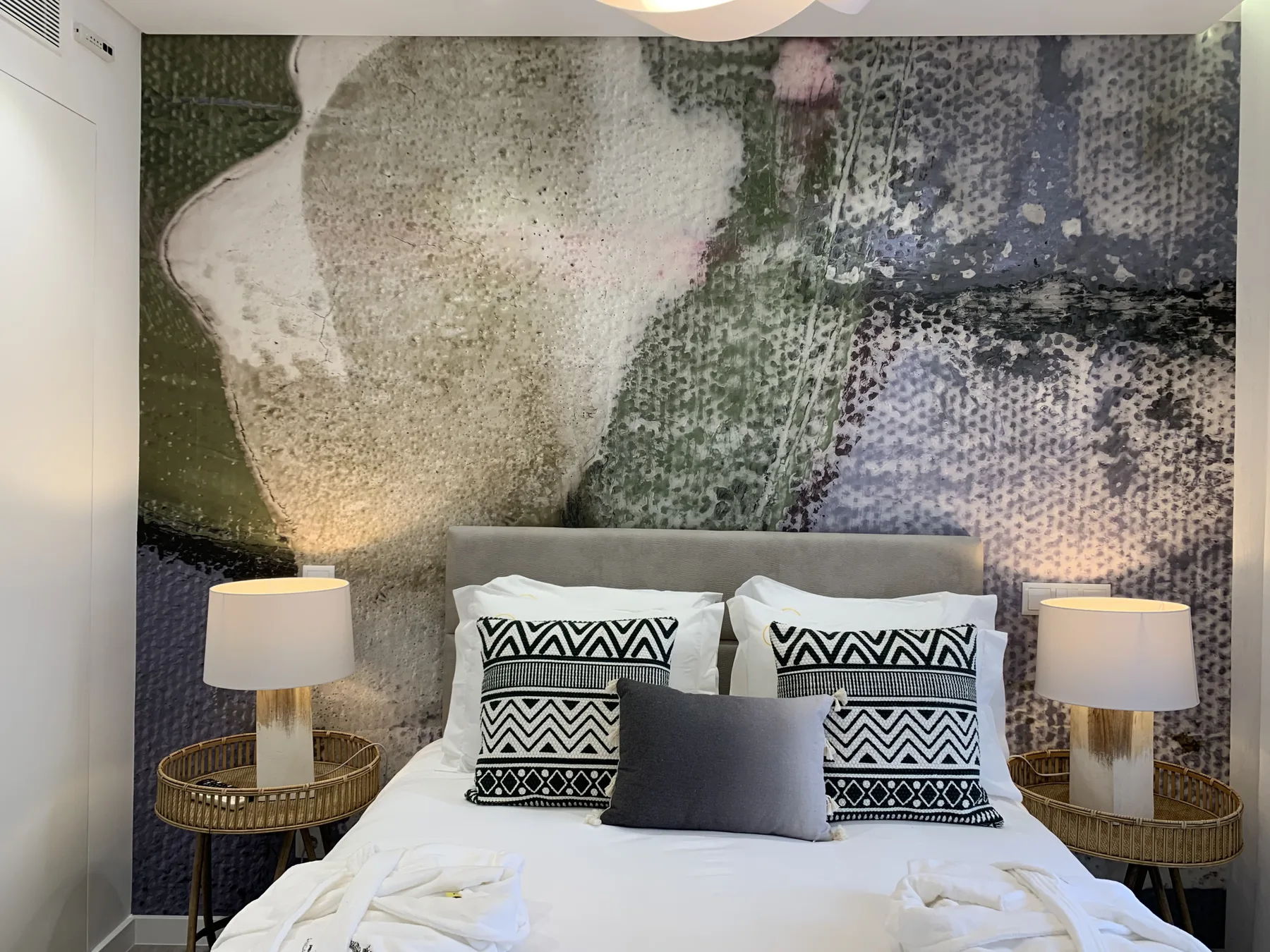 Un dormitorio con una cama bien tendida, cojines estampados y un gran mural en la pared.