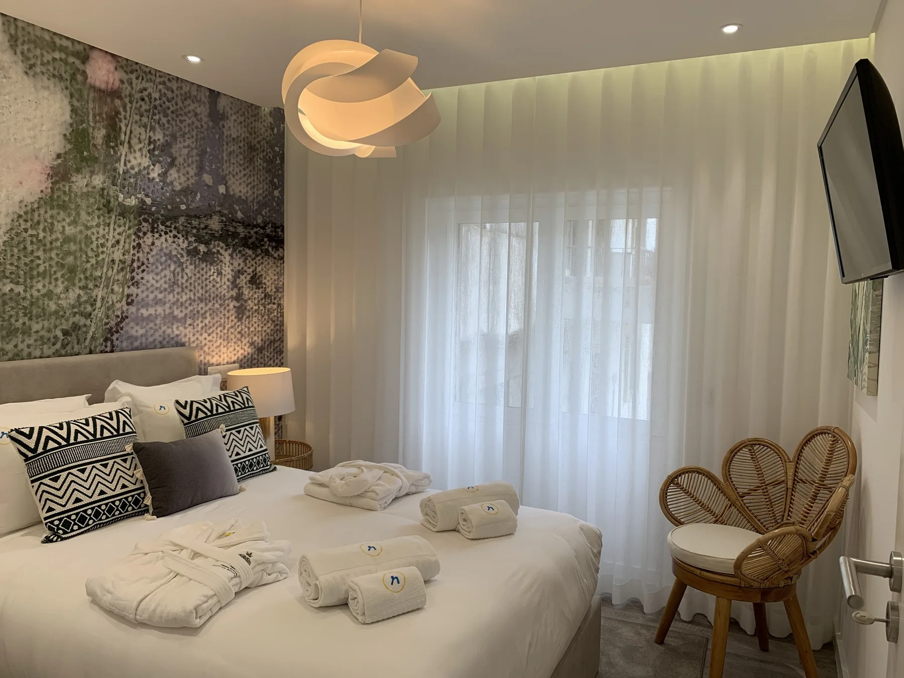 Un dormitorio con una cama bien hecha y cortinas translúcidas en la ventana.