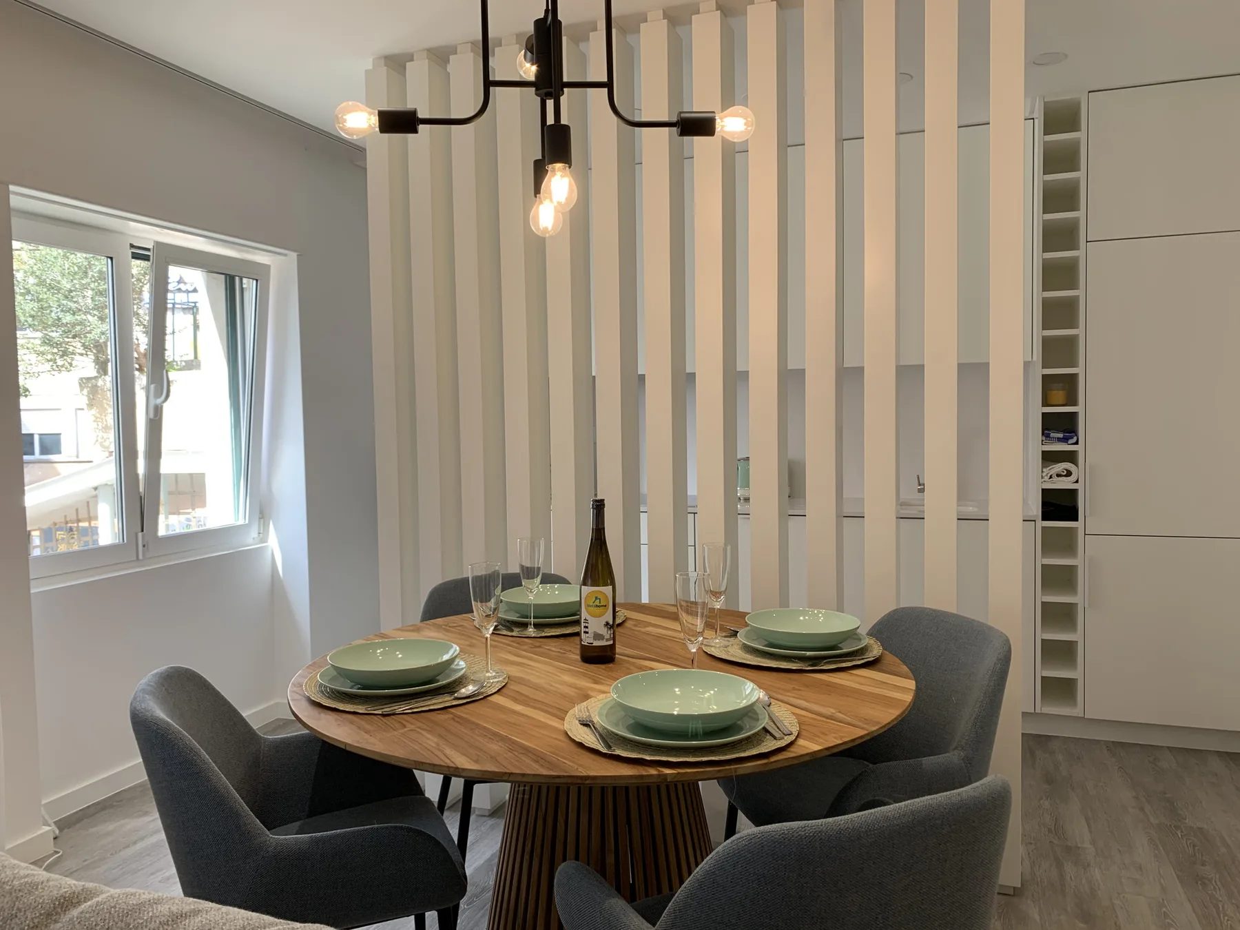 Comedor con una mesa redonda de madera puesta con platos bajo una lámpara colgante.