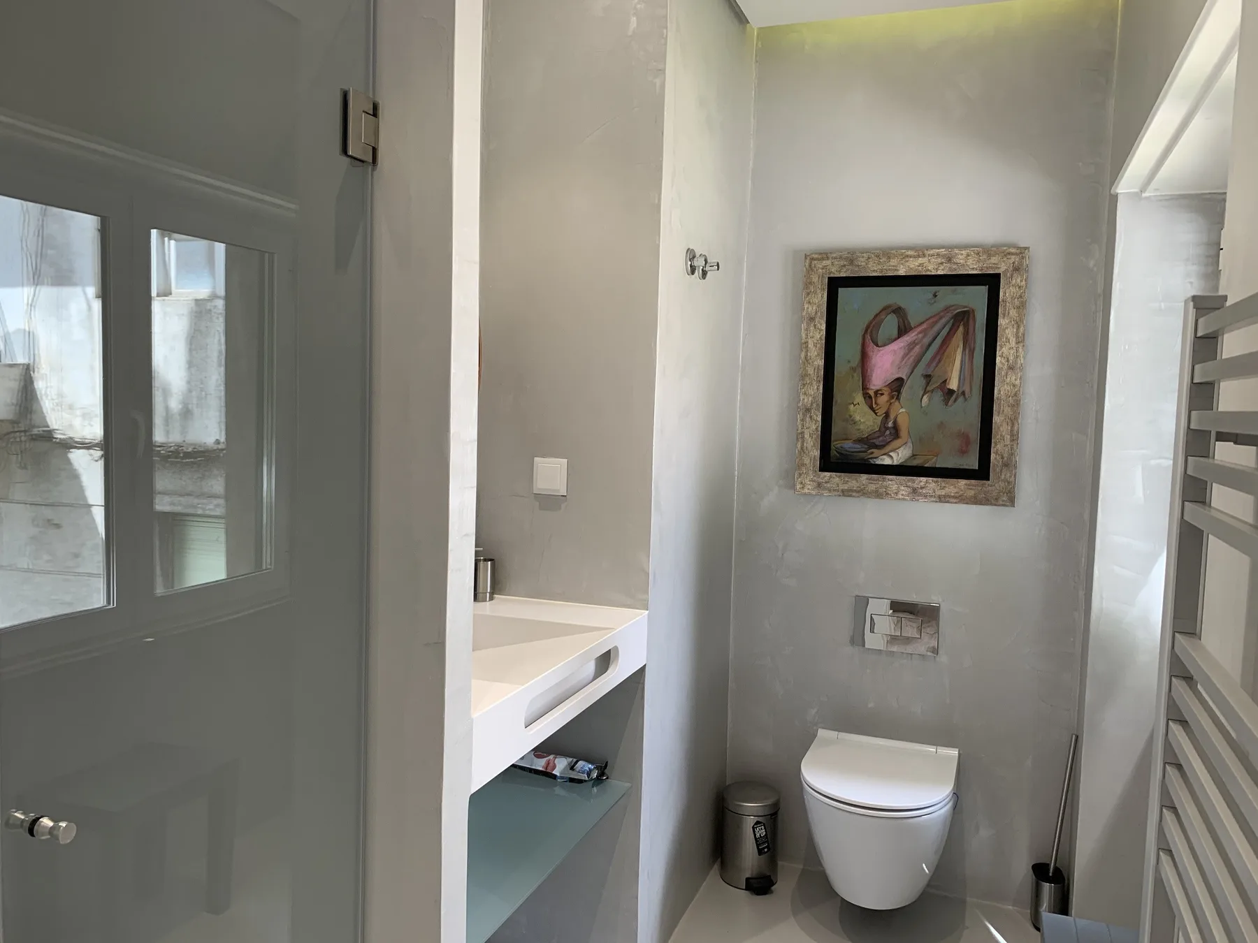 Un baño con inodoro suspendido, lavabo y una lámina enmarcada.