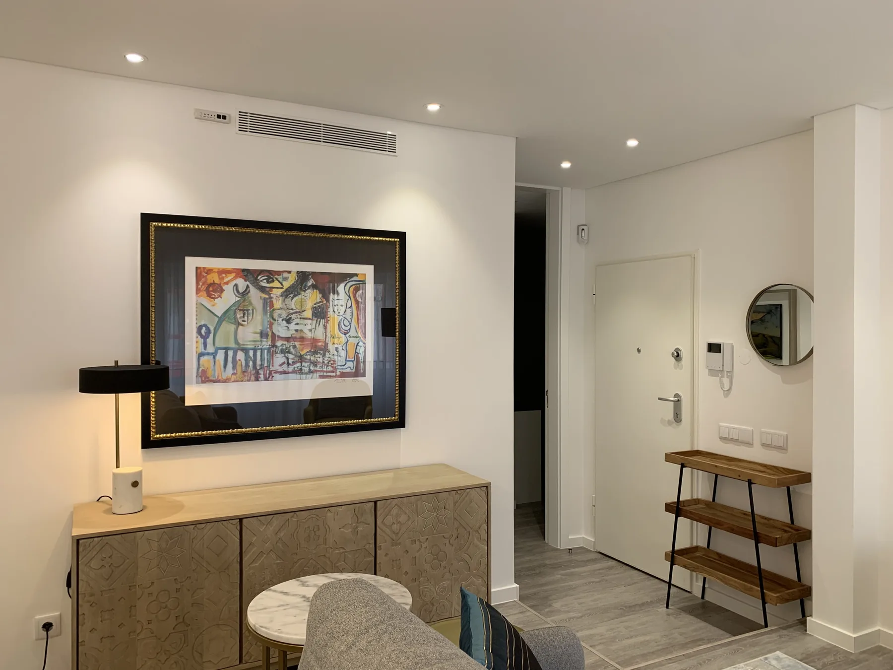 Una entrada de apartamento moderna con una obra enmarcada y una consola de madera.
