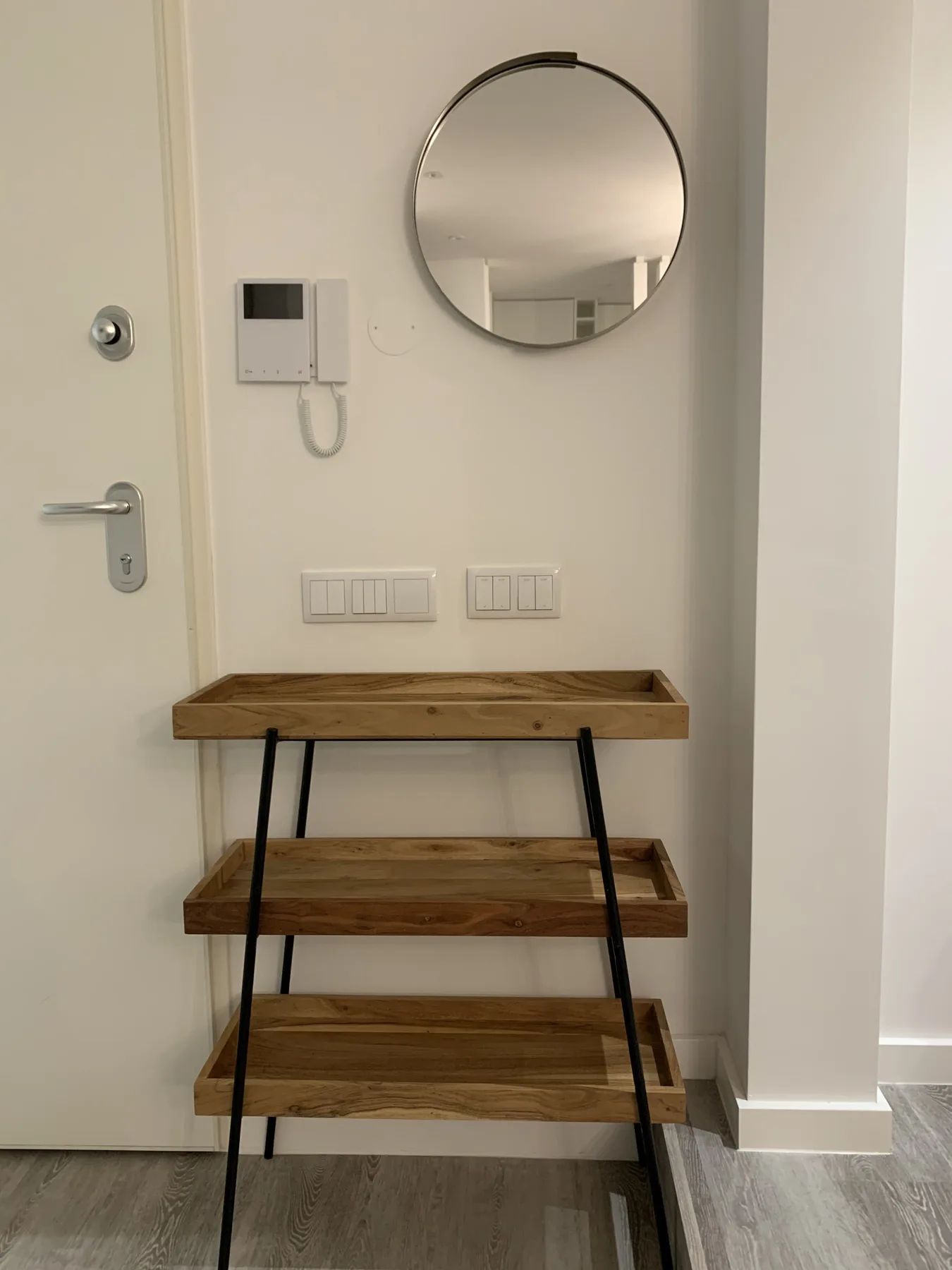 Una entrada tiene un espejo redondo en la pared sobre una estantería de madera.