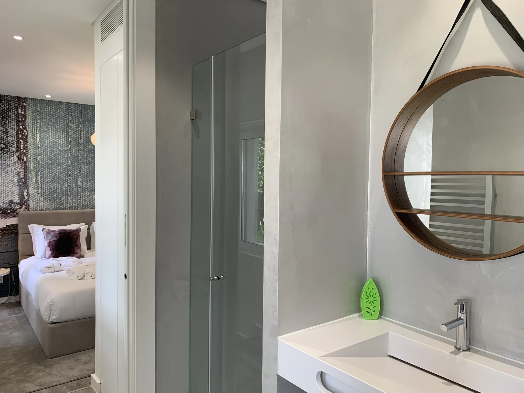 Un baño con lavabo y espejo redondo, con un dormitorio visible al fondo.