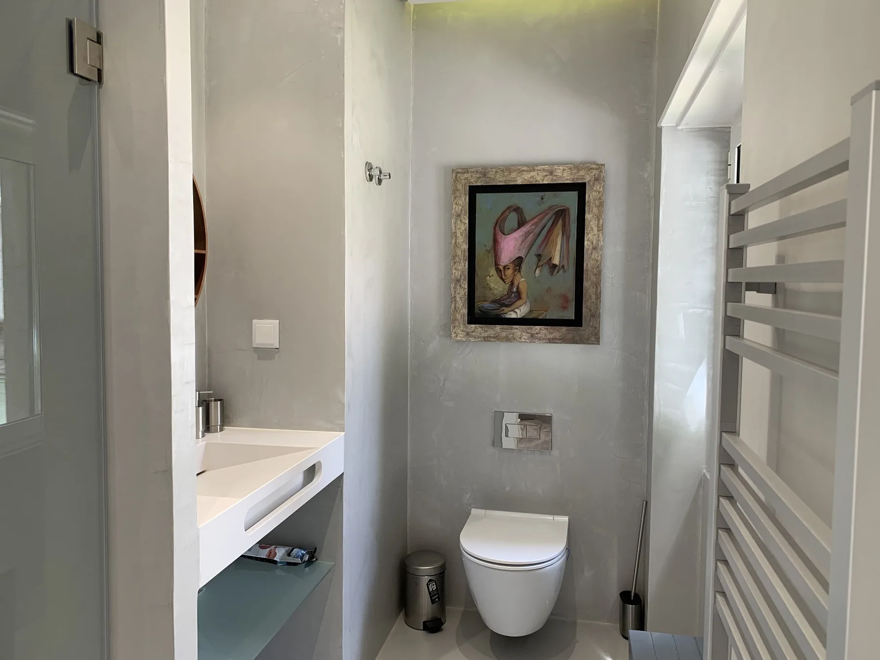 Un baño con inodoro suspendido, lavabo y una obra enmarcada.
