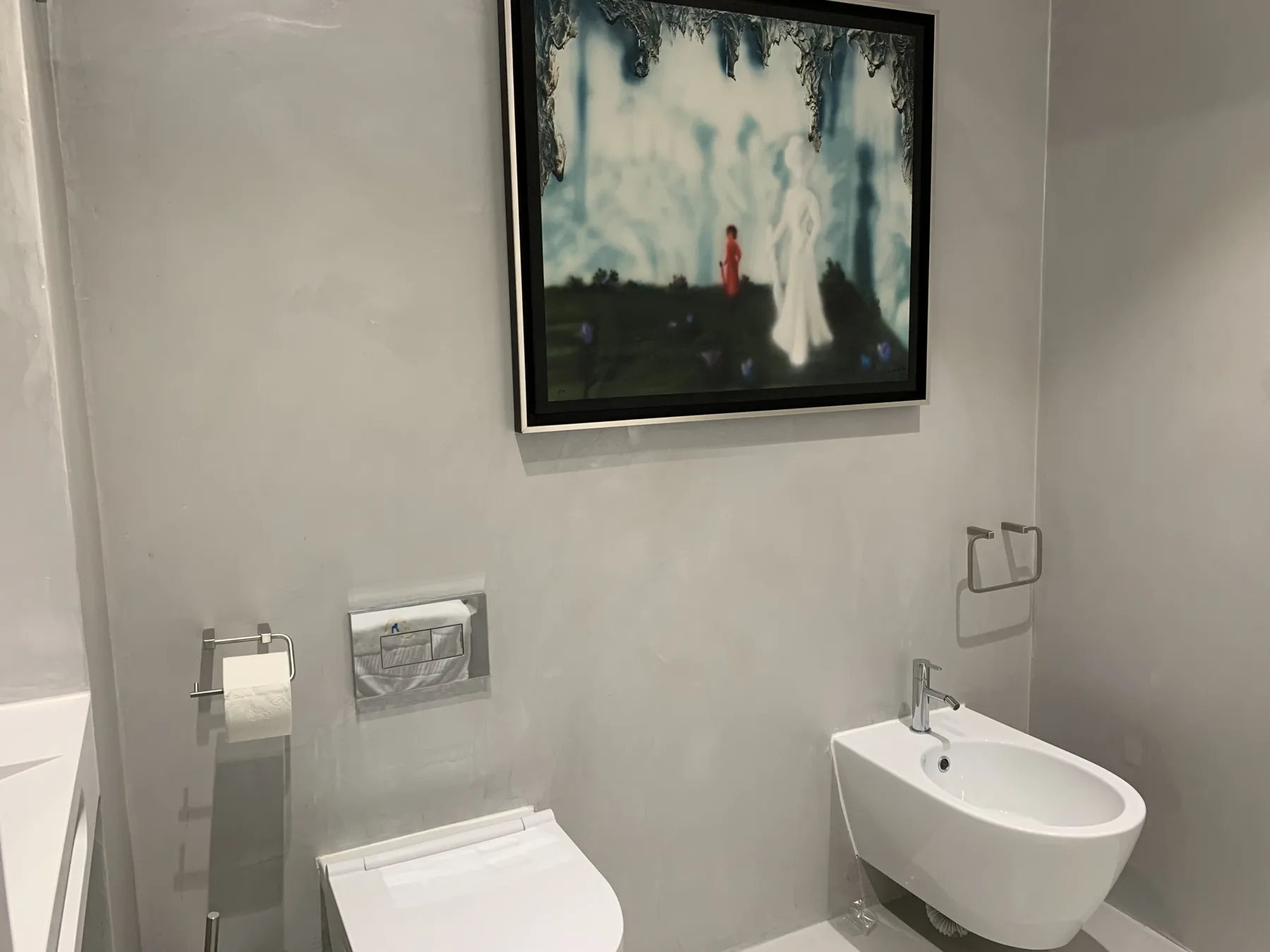 Un baño con un inodoro suspendido y una obra enmarcada encima.