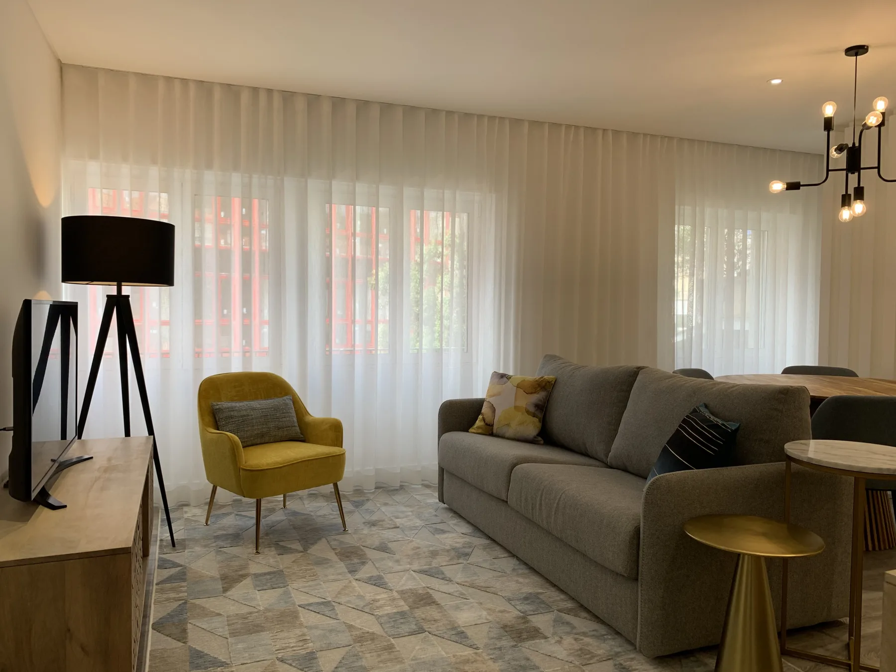 Sala de estar con asientos, un televisor y ventanales con cortinas.