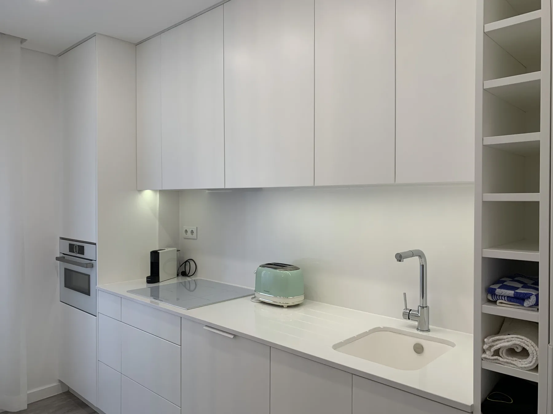 Una cocina blanca y luminosa con placa de cocción, encimera y fregadero.