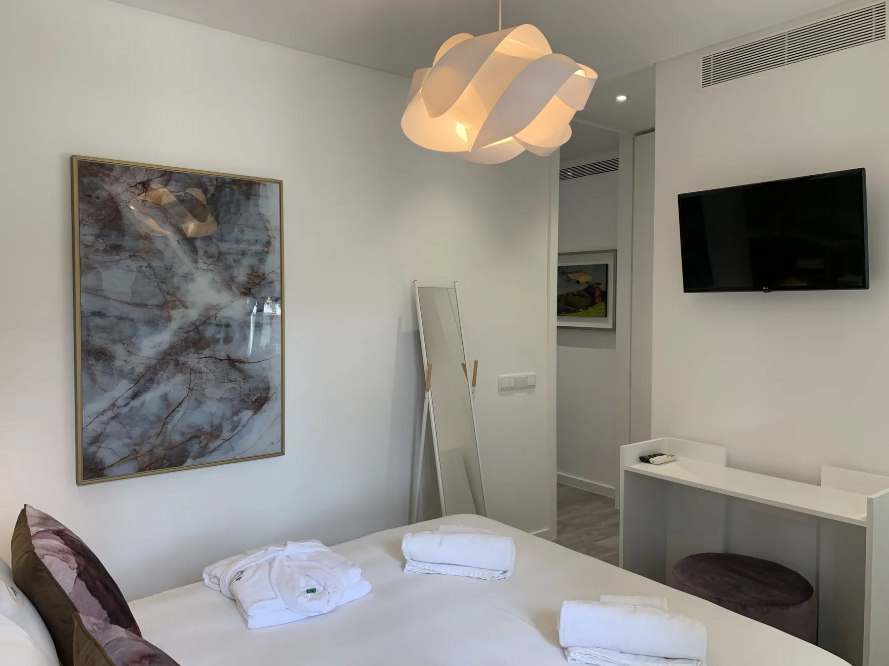 Un dormitorio con una cama, toallas dobladas y un televisor en la pared.