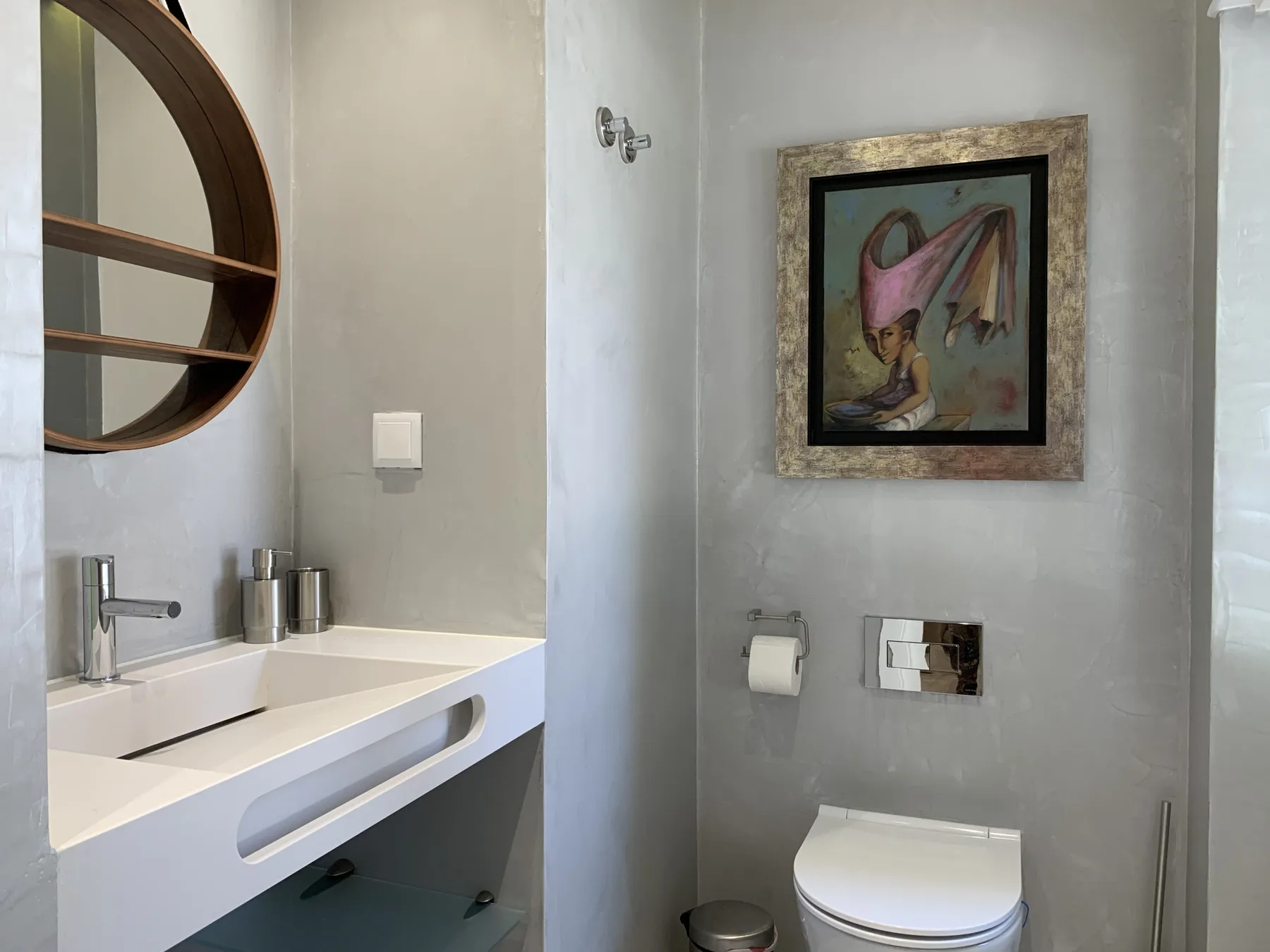 Un baño con lavabo, inodoro y una obra enmarcada en la pared.