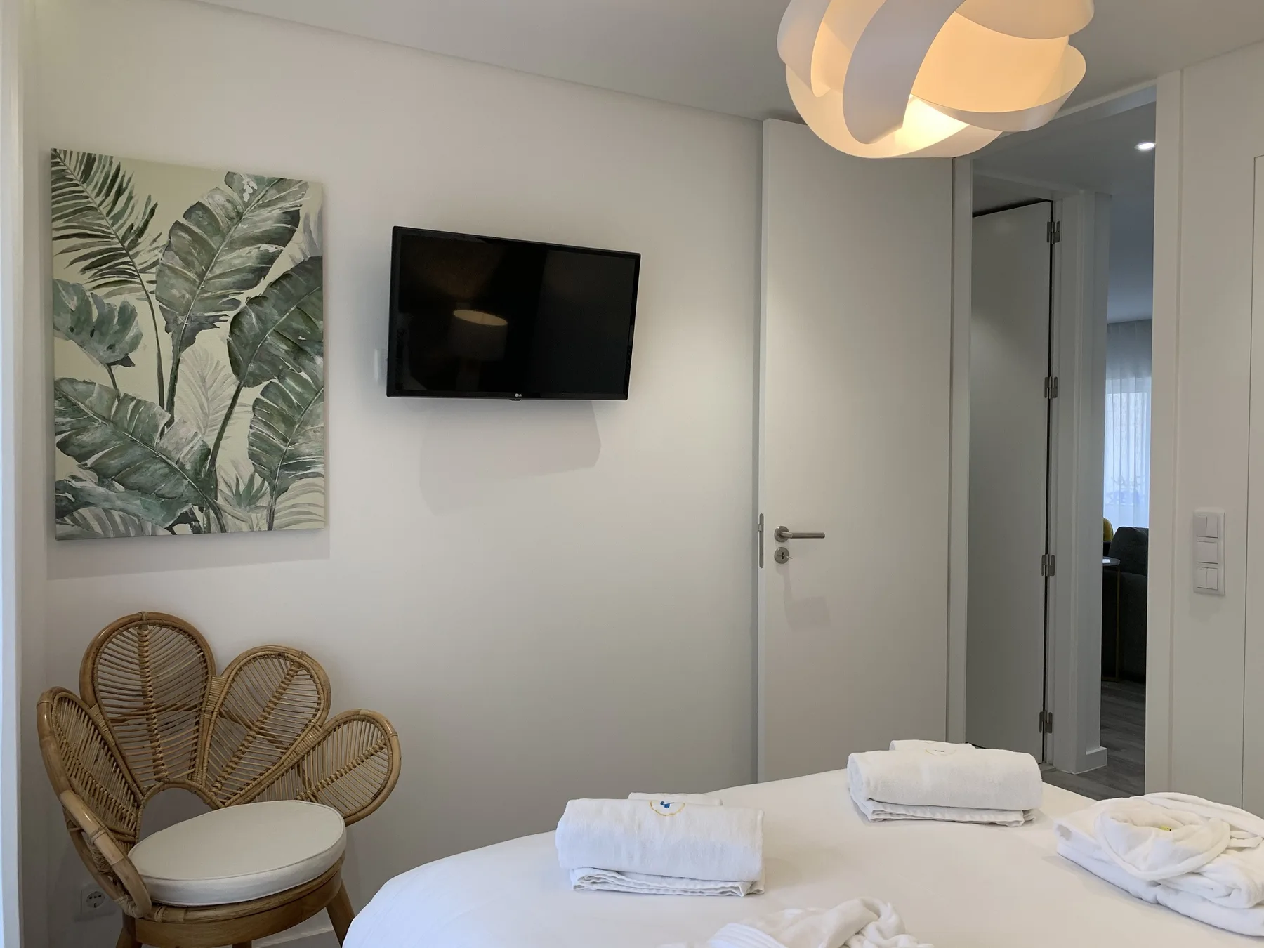 Un dormitorio luminoso con un televisor en la pared y un cuadro de hojas.