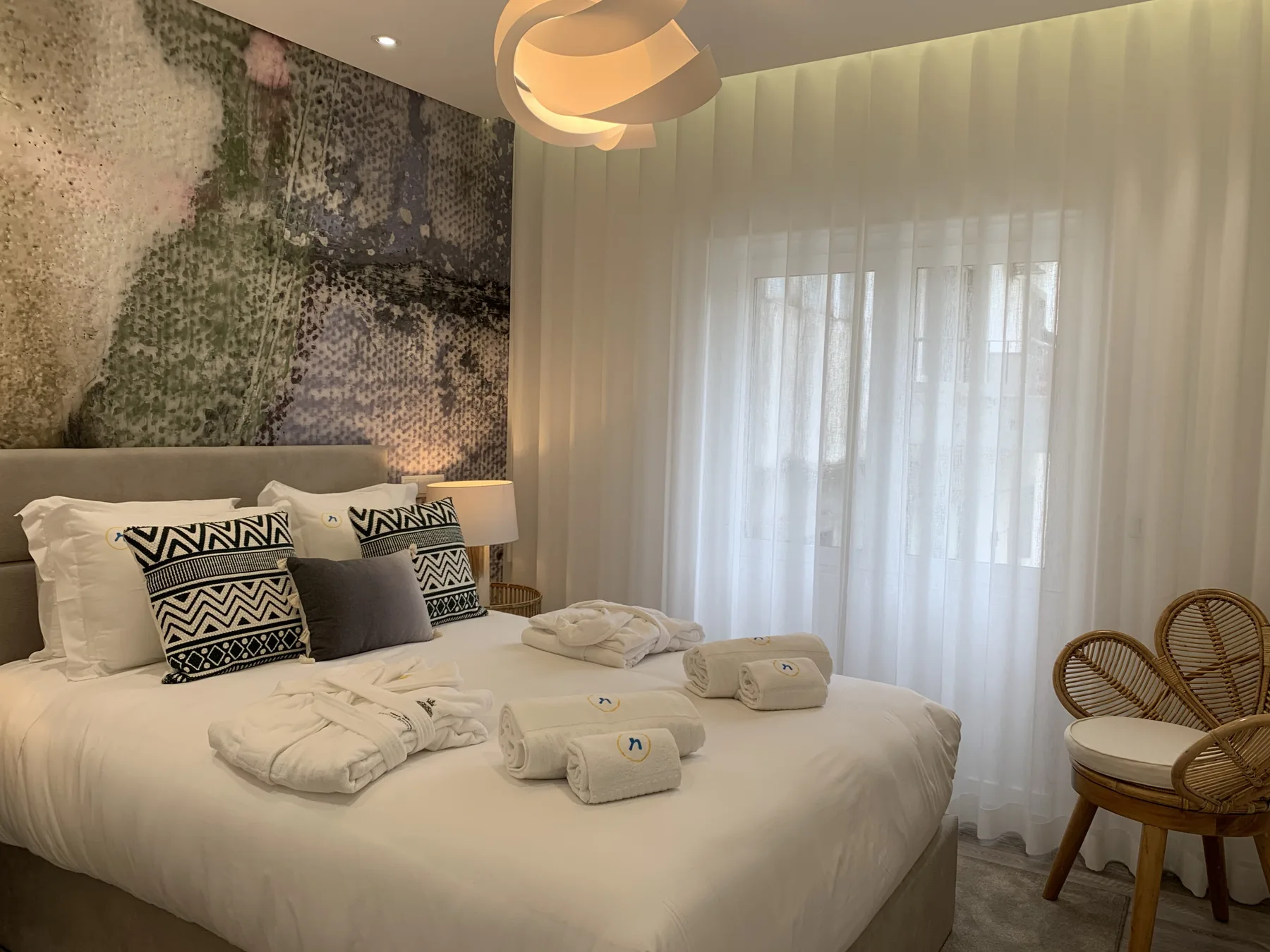 Dormitorio con una cama bien hecha y cortinas translúcidas en la ventana.