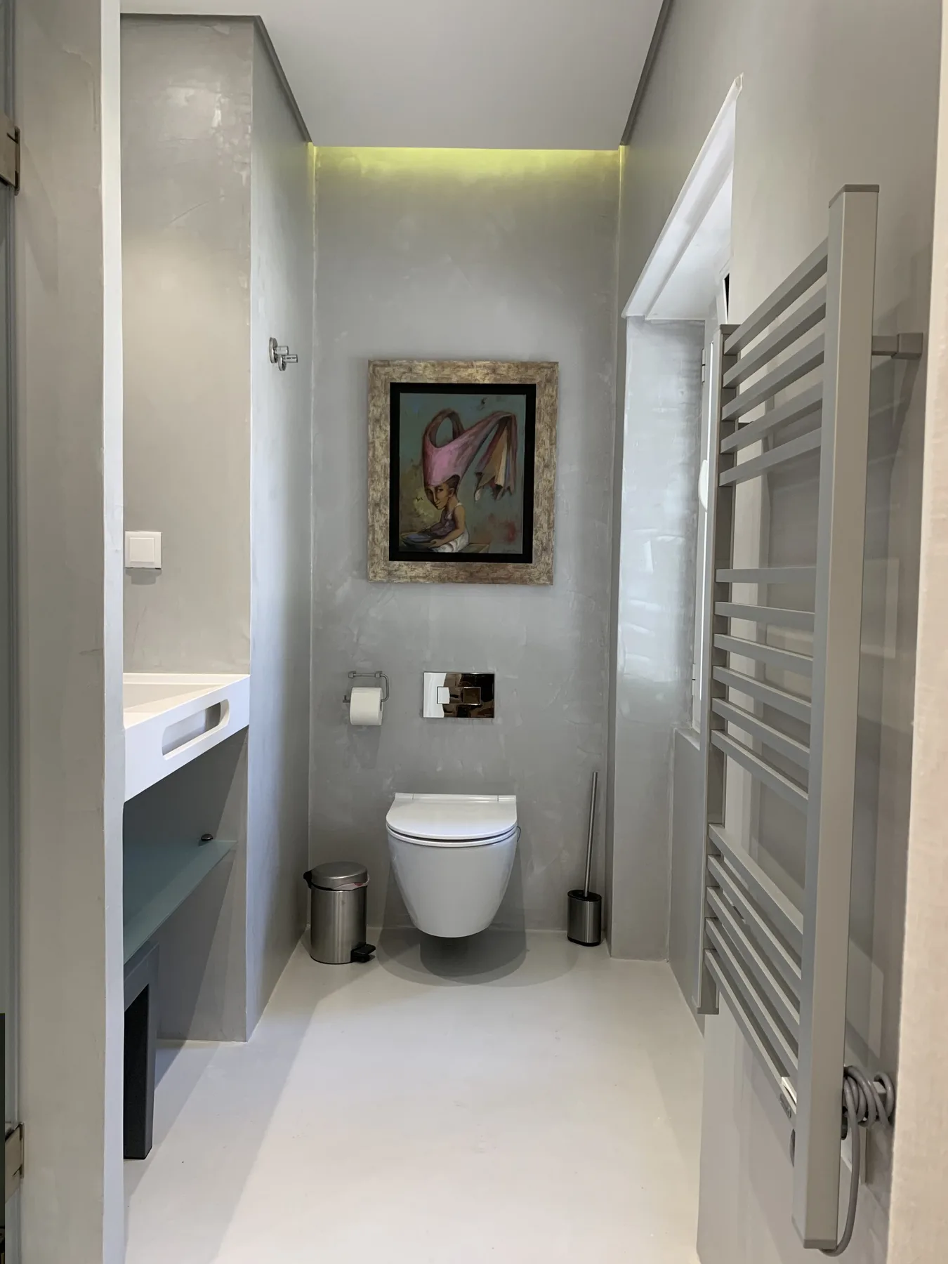 Un baño moderno con un inodoro suspendido y una obra enmarcada.