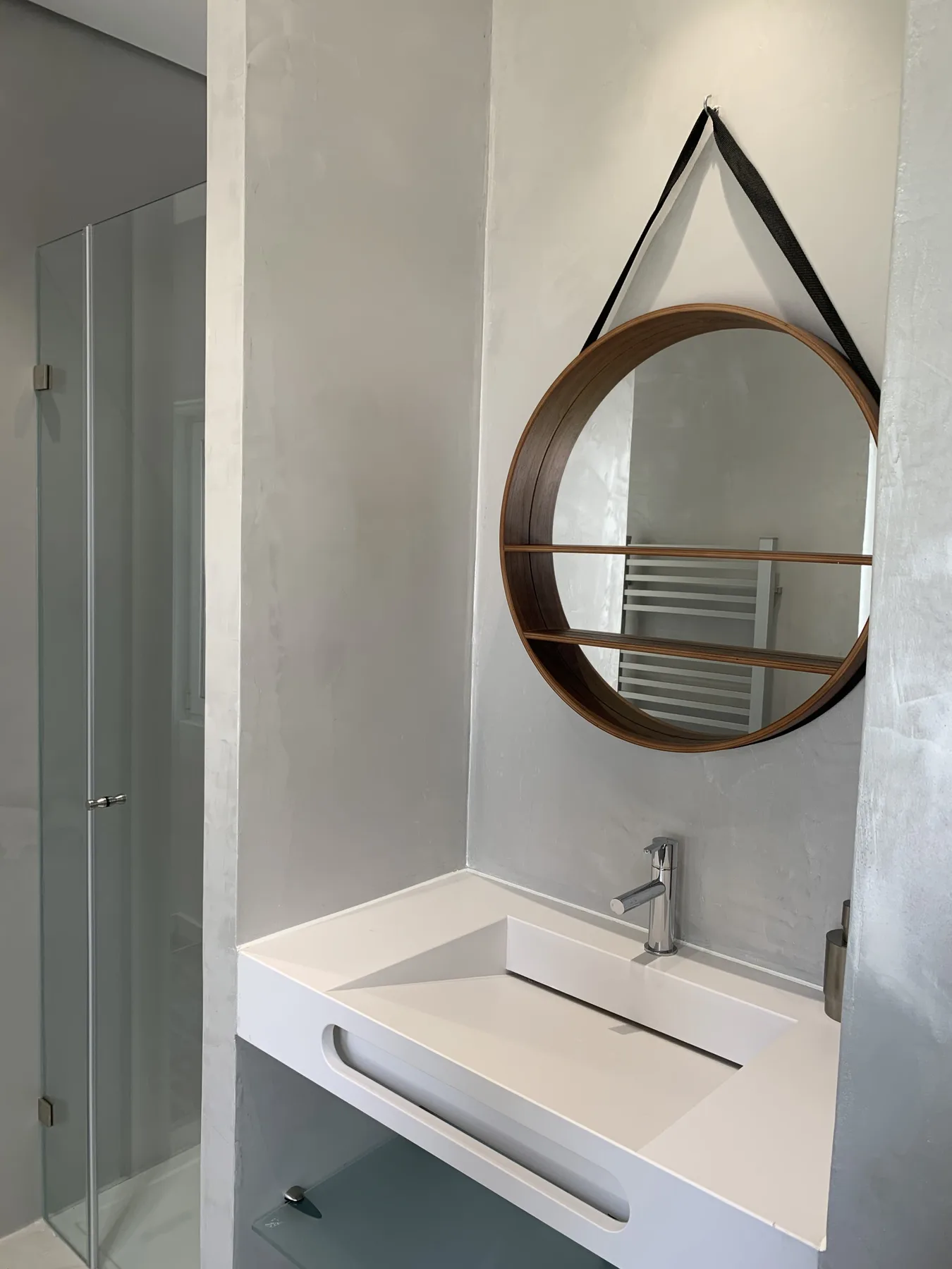 Un tocador de baño moderno con un espejo redondo y una ducha de cristal.