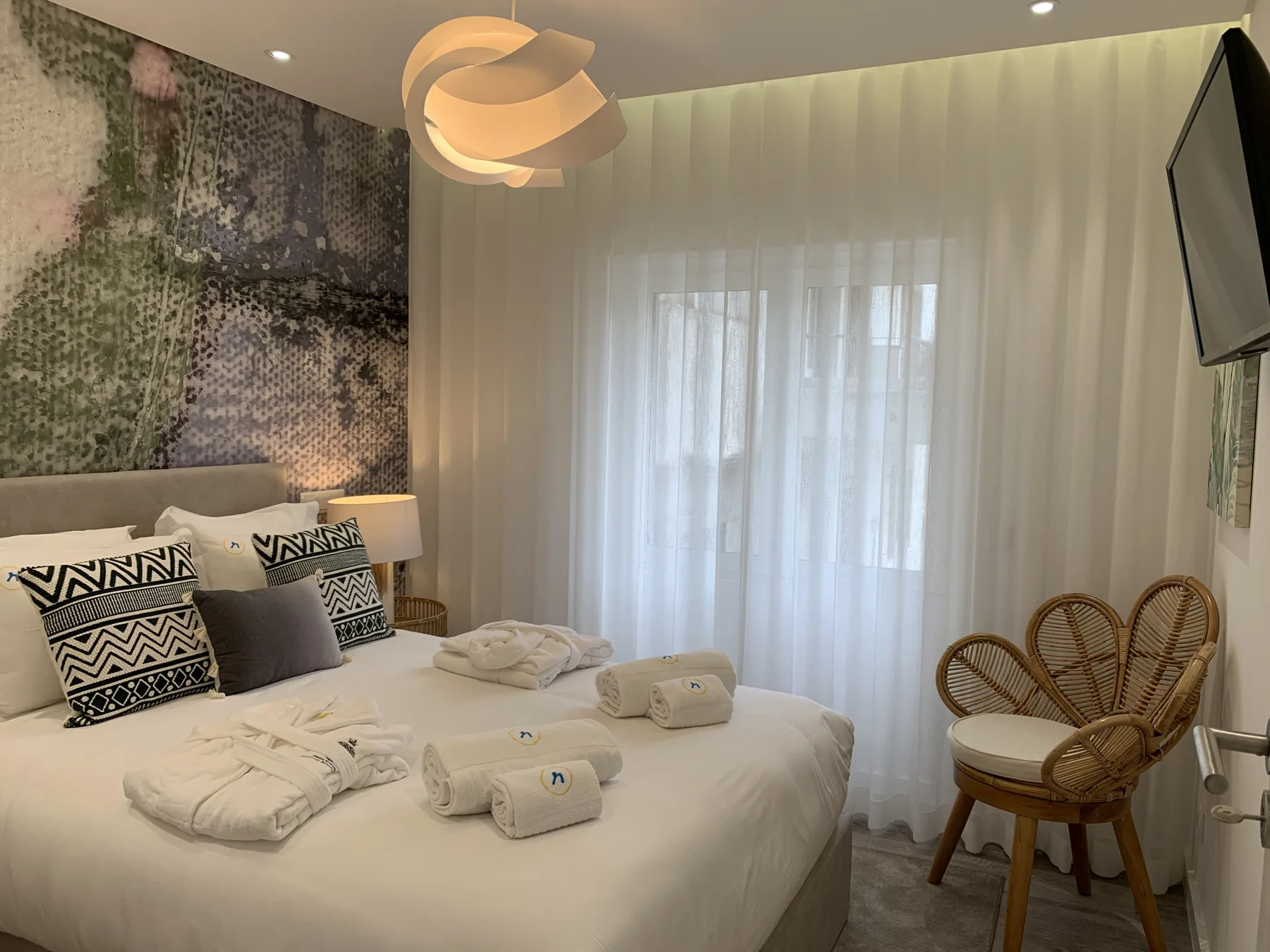 Un dormitorio con una cama bien tendida y cortinas translúcidas en la ventana.