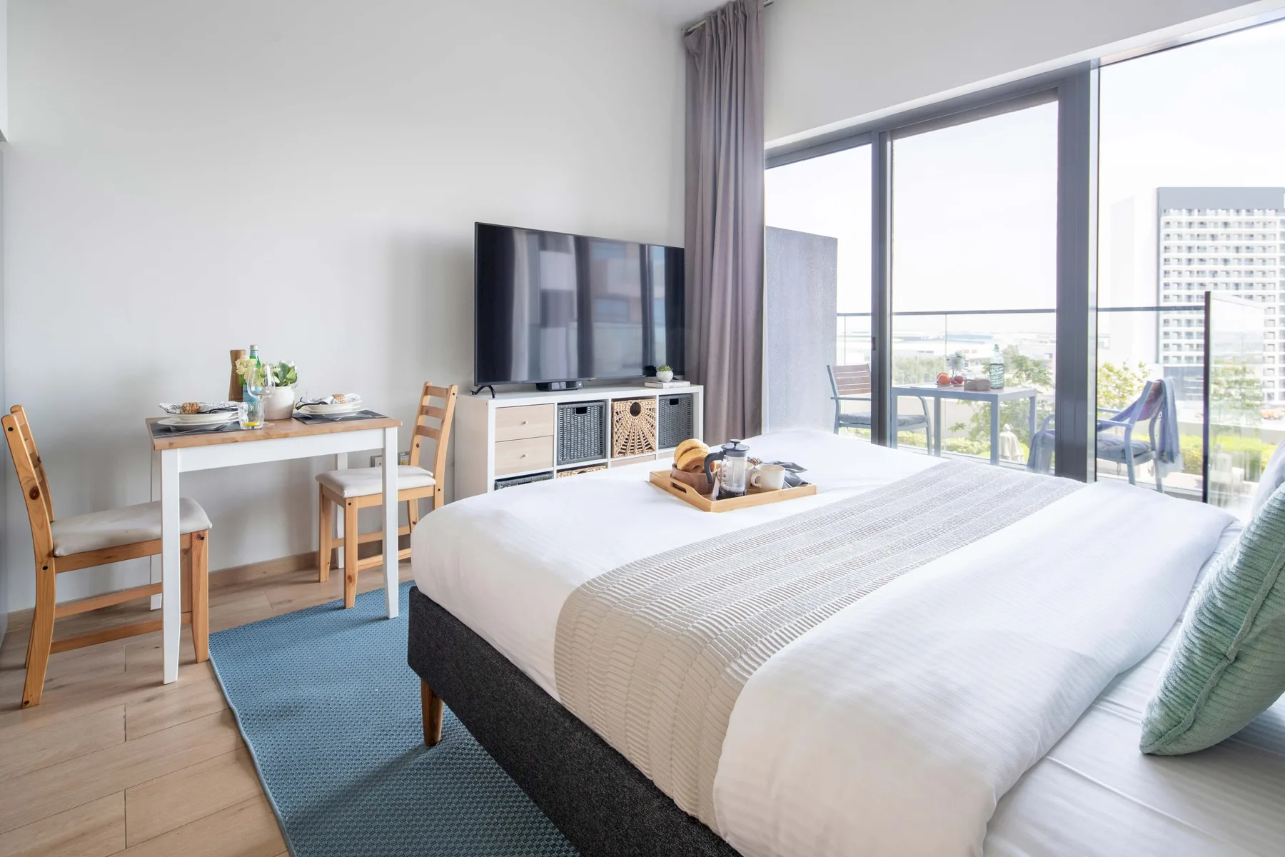 A bright bedroom with a large bed, a television, and floor-to-ceiling windows.