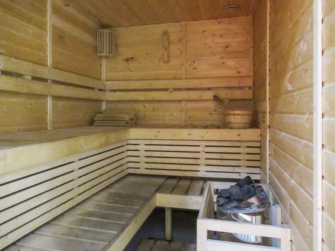 A wood-paneled sauna with tiered wooden seating and a metal heater.