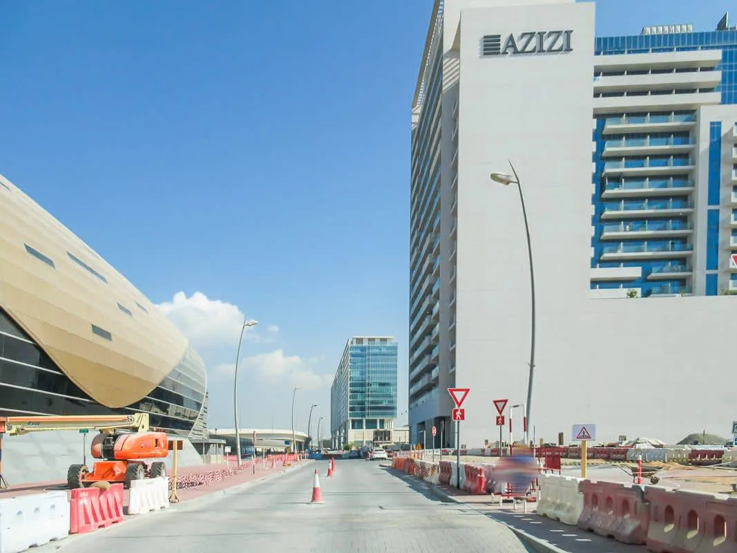 A city street runs between modern buildings, with road barriers lining the construction area.