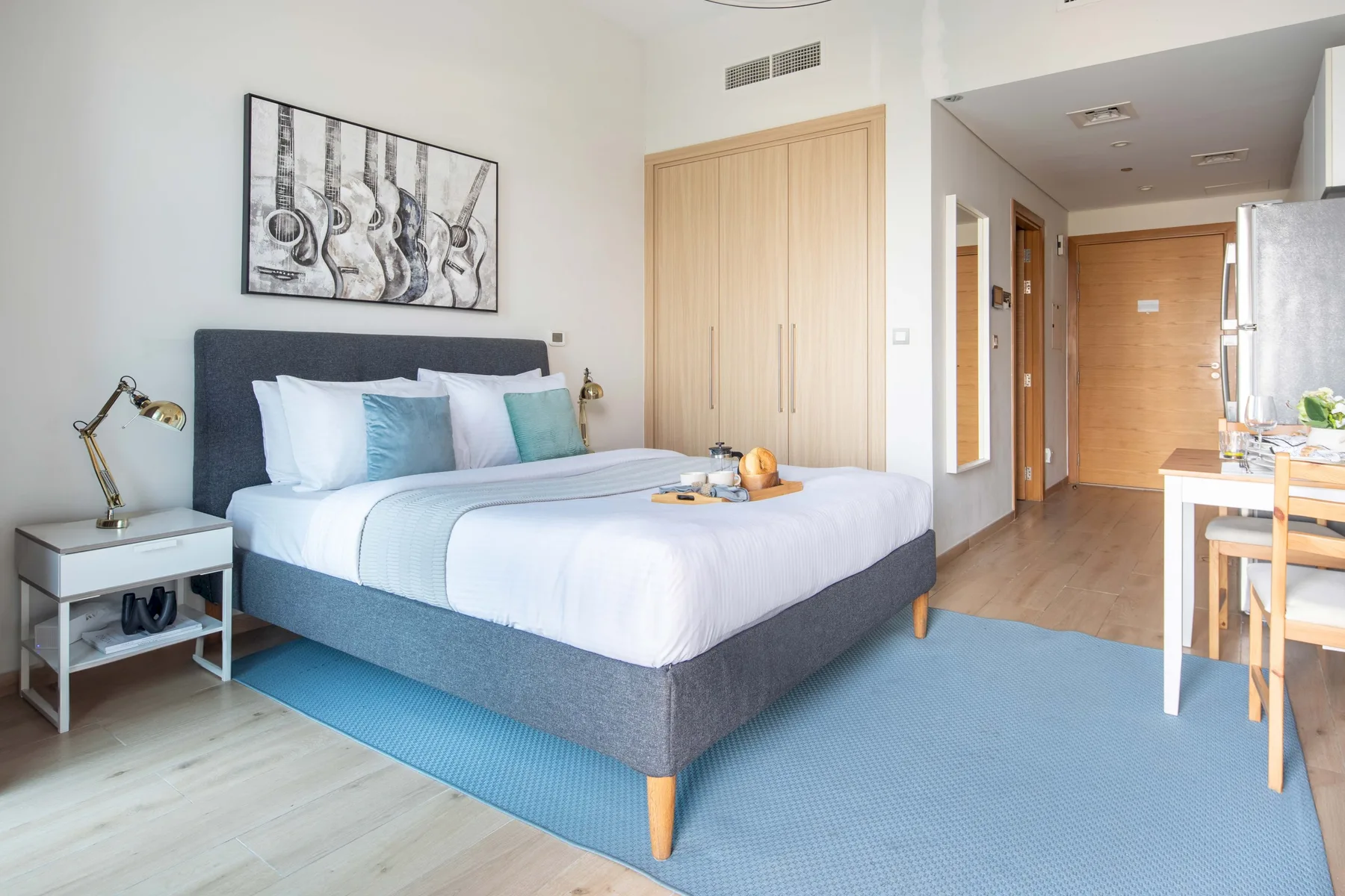 A bedroom with a neatly made bed, bedside table, and blue rug.