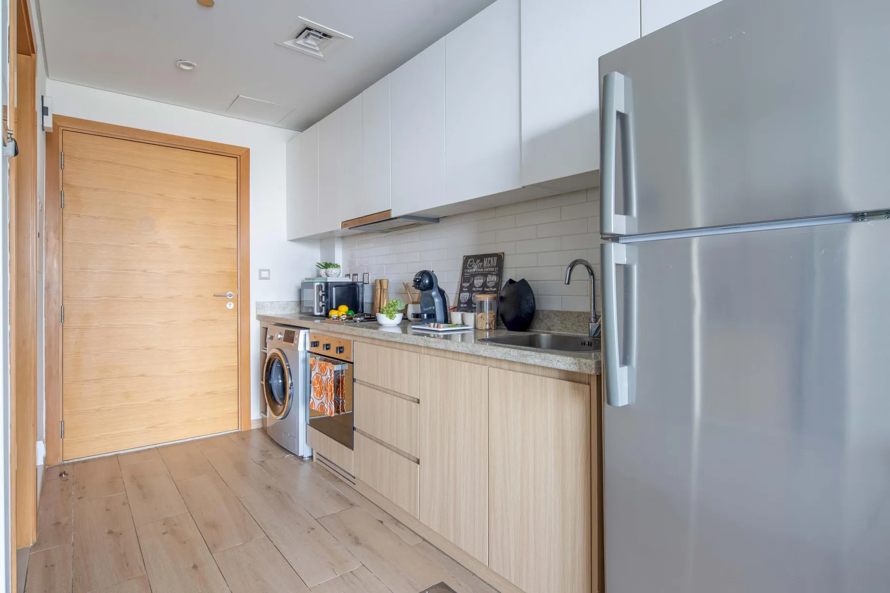A modern kitchen with light wood cabinets, a refrigerator, and countertop appliances.