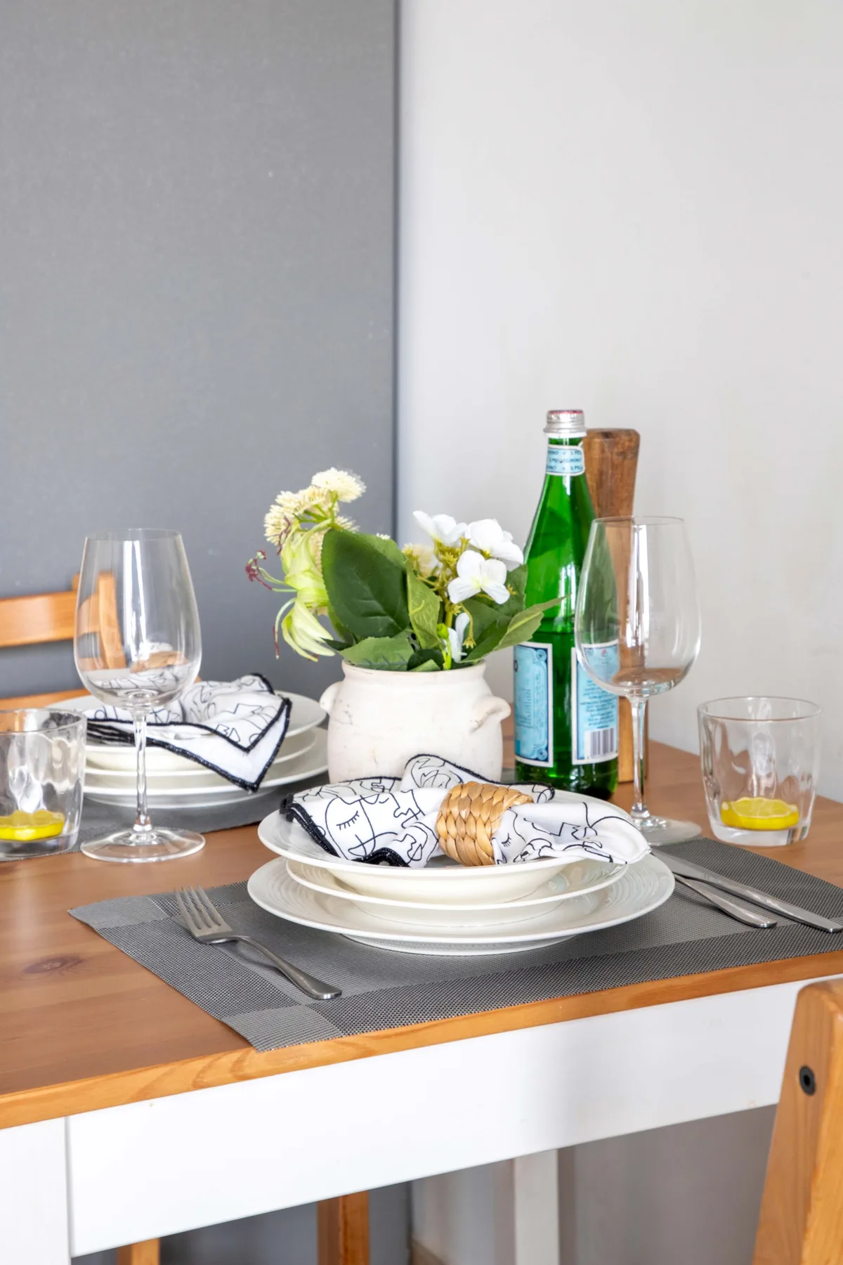 A dining table is set with plates, glasses, and a vase of flowers.
