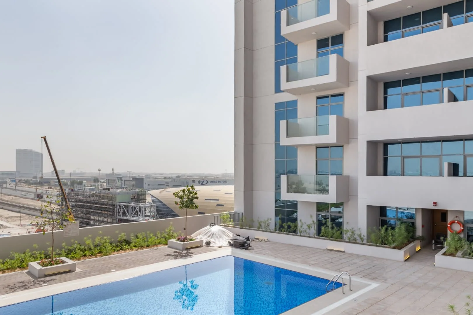 A rooftop swimming pool sits beside a modern building and a planted terrace.