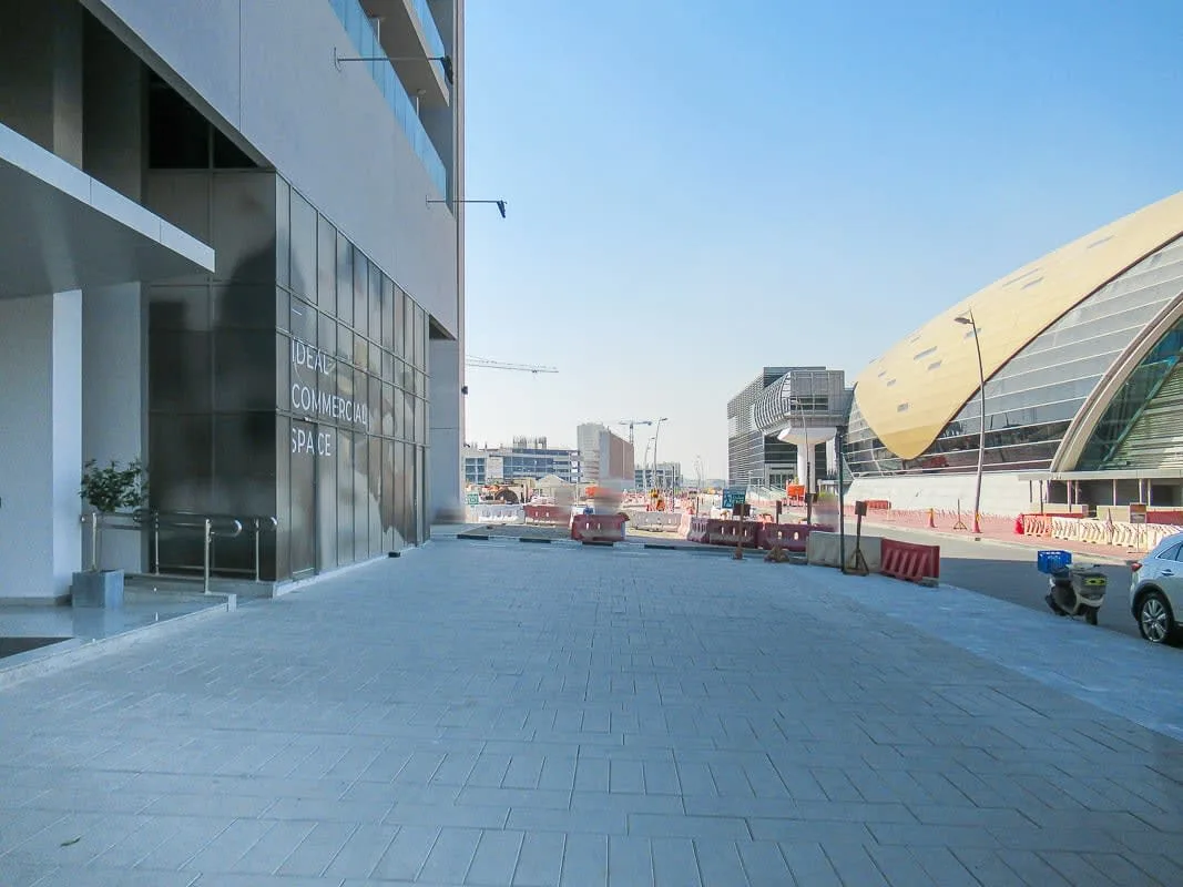 A paved pedestrian plaza runs between a glass-fronted building and a curved-roof structure.