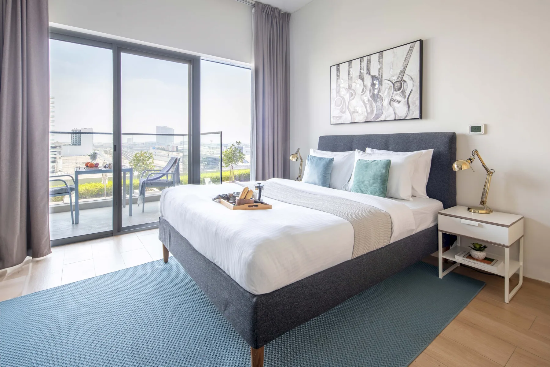 A bright bedroom with a large bed beside floor-to-ceiling windows.