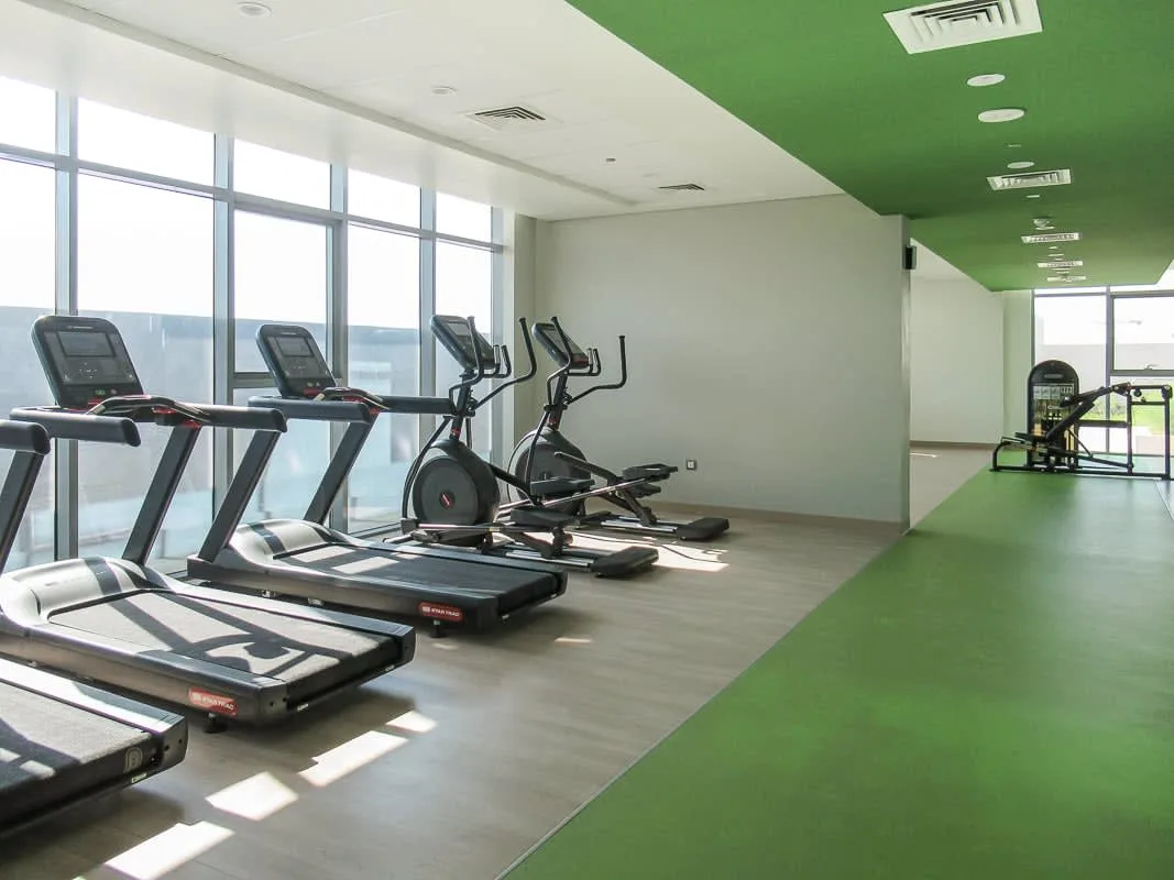 A gym with cardio exercise machines beside large windows.