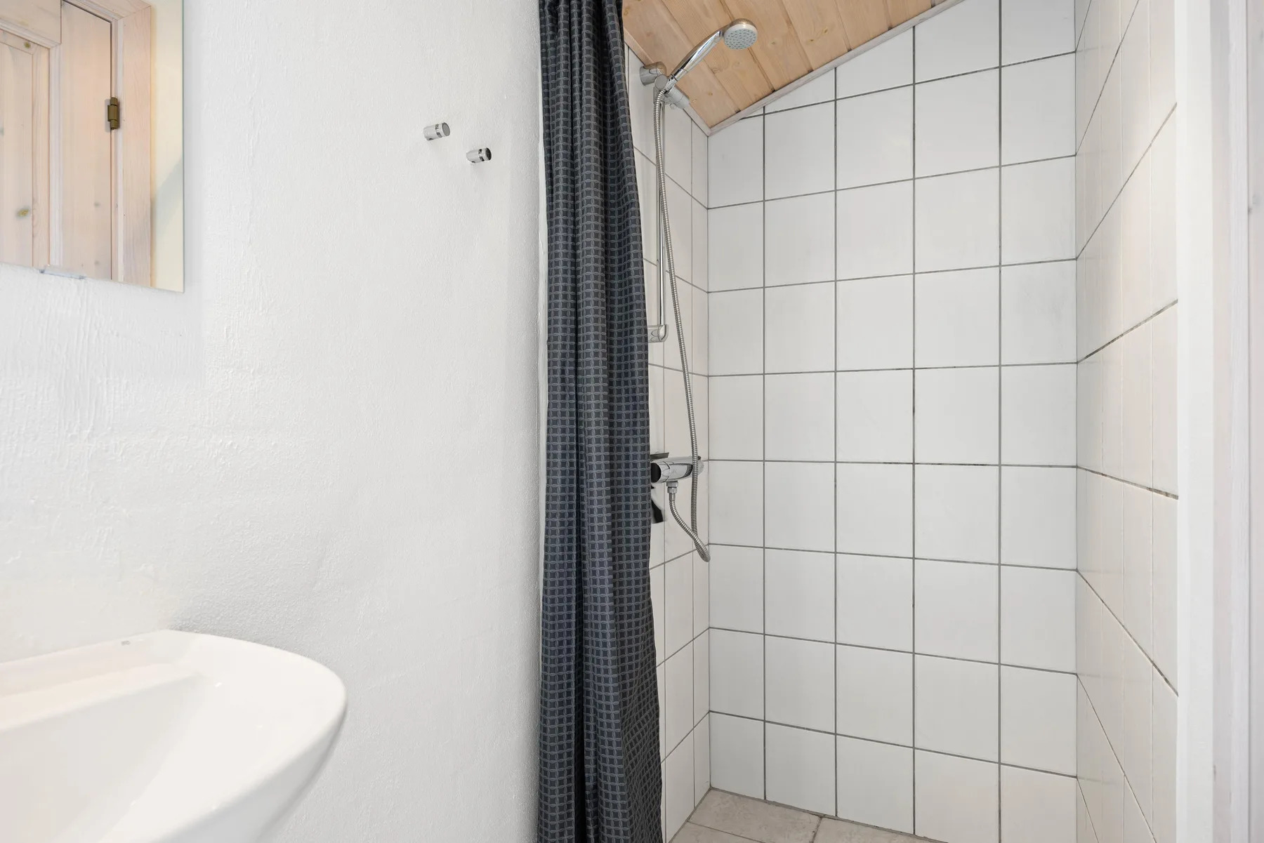Un baño con una zona de ducha alicatada y una cortina oscura.