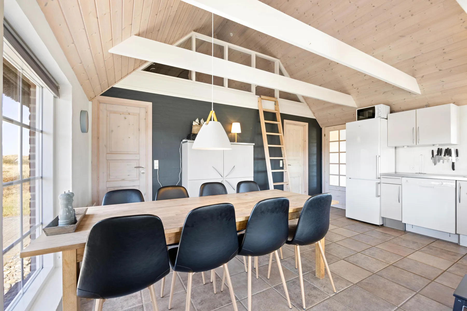 Comedor y cocina con una mesa larga bajo un techo inclinado de madera.