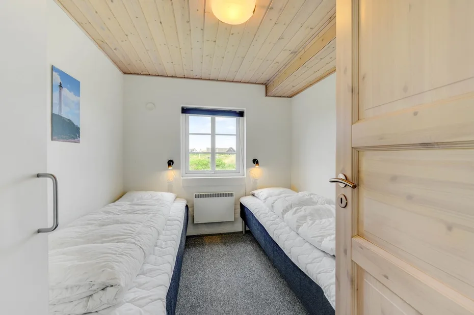 Un dormitorio compacto tiene dos camas frente a una ventana con vistas a la vegetación.