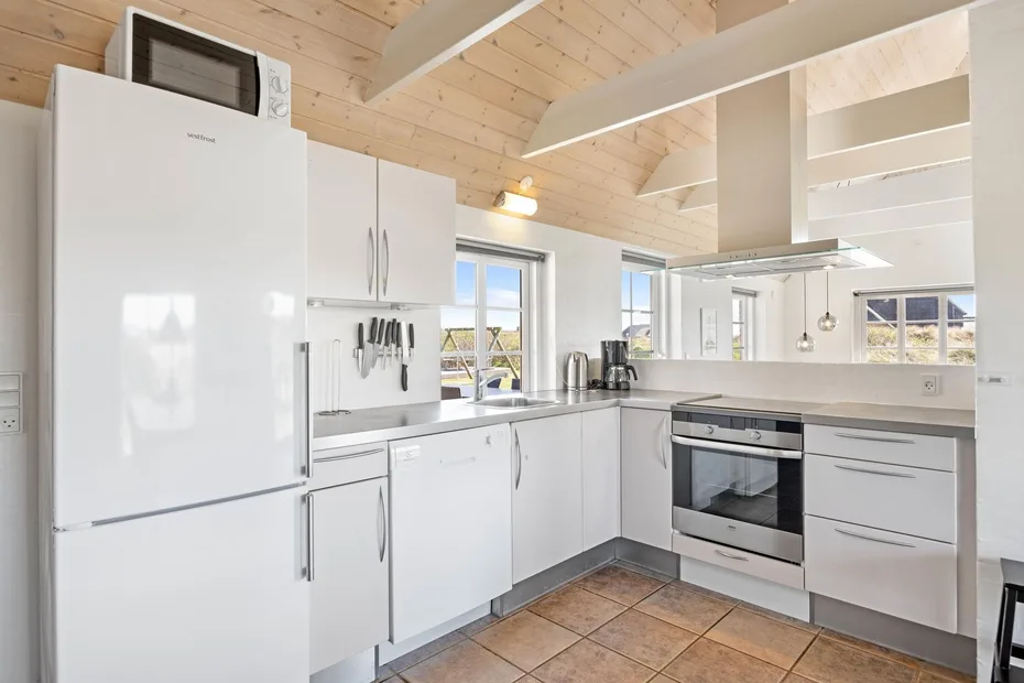 Una cocina luminosa con gabinetes blancos, un refrigerador y una zona para cocinar.
