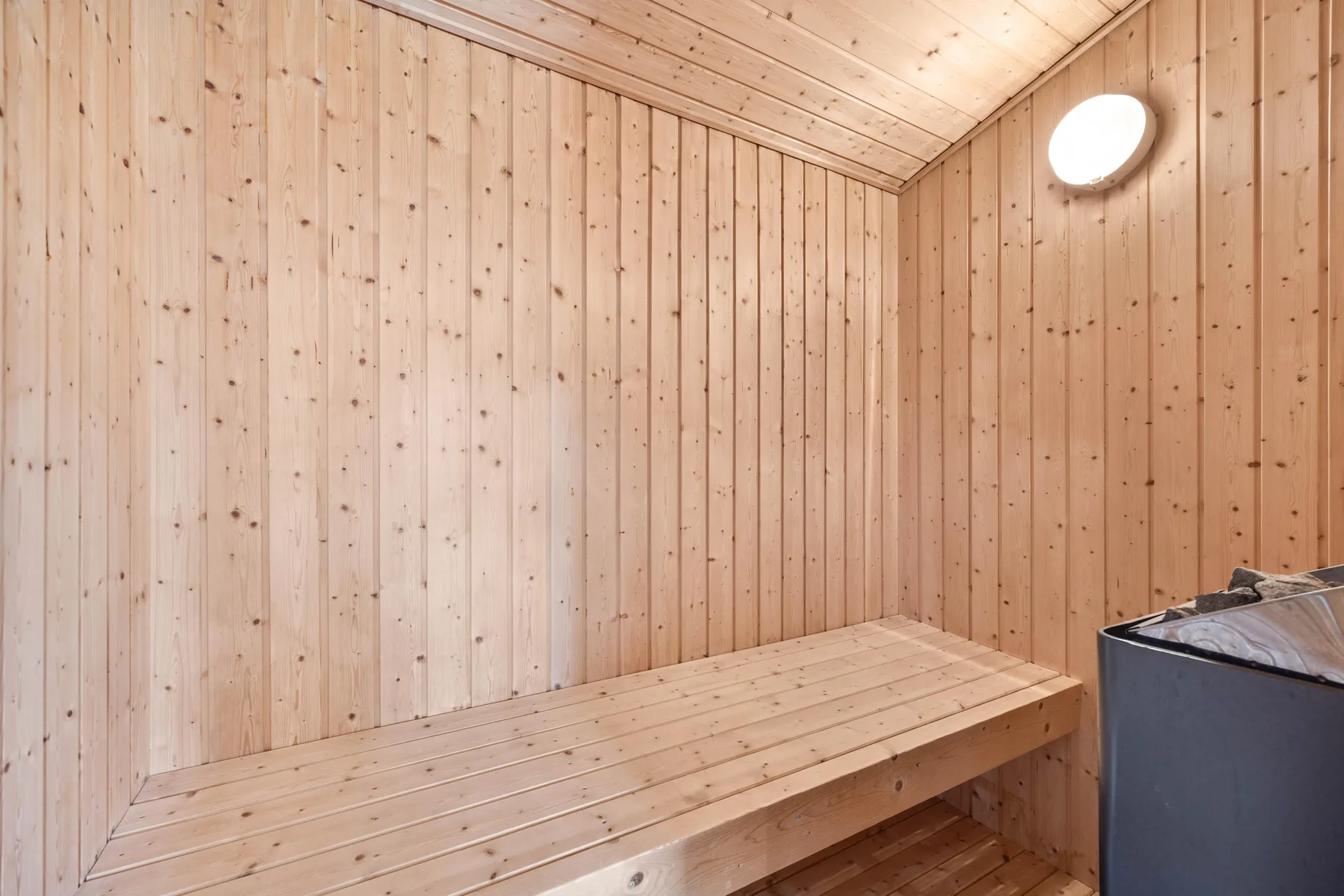Una sauna revestida de madera con un banco largo y un calefactor.
