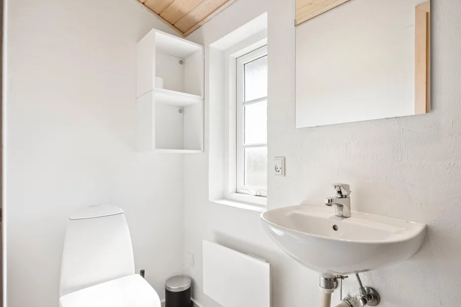 Un baño luminoso con lavabo de pared, espejo y ventana.