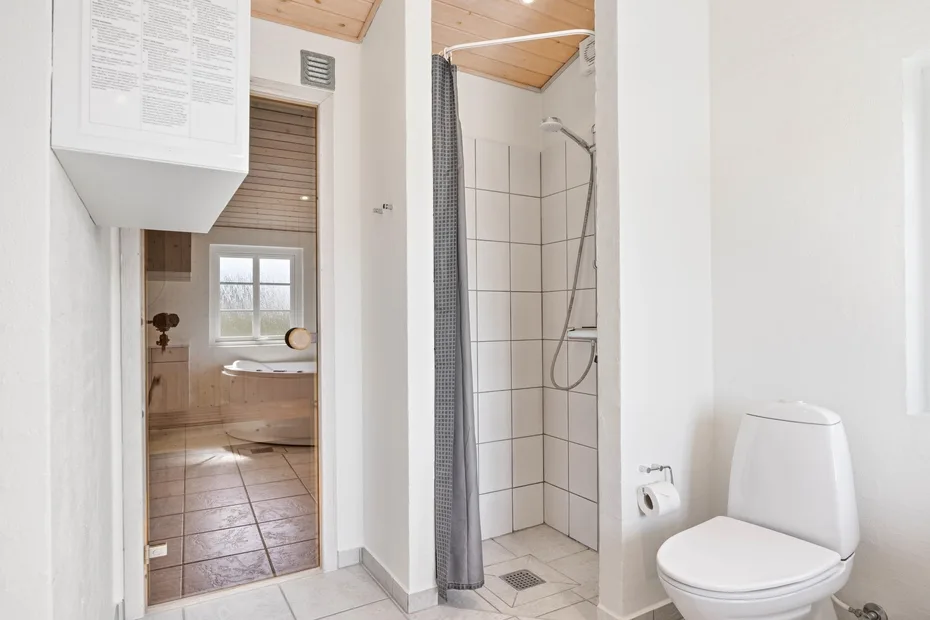 Un baño alicatado con ducha, inodoro y una puerta a una habitación con lavabo.