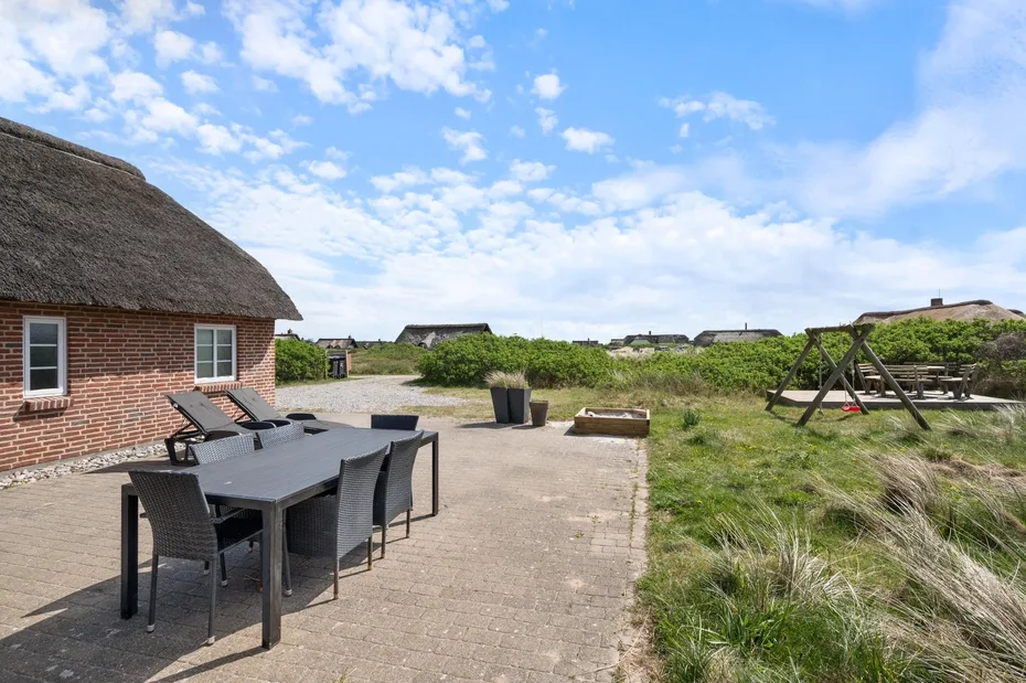 Un patio al aire libre con una mesa de comedor junto a un edificio con techo de paja.