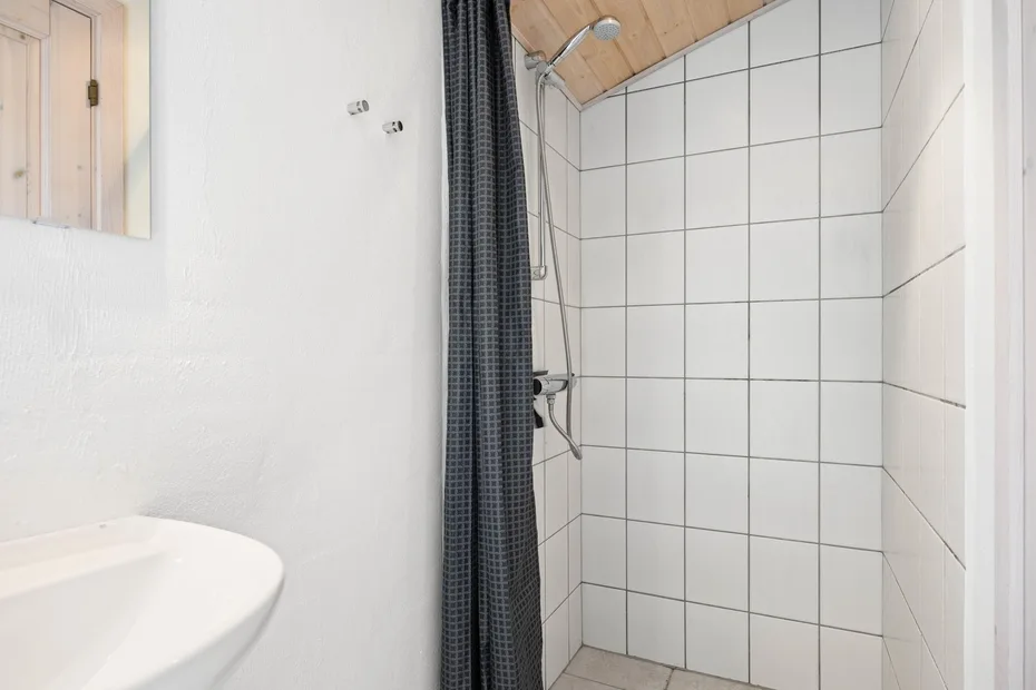 Un baño con una ducha de azulejos y una cortina oscura junto a un lavabo.