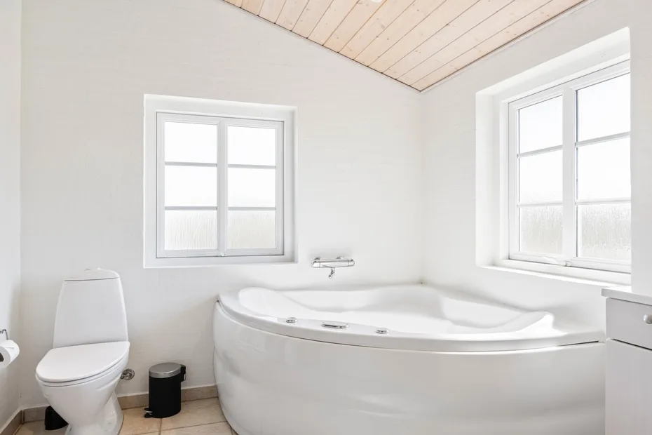 Un baño luminoso con una bañera grande bajo dos ventanas.