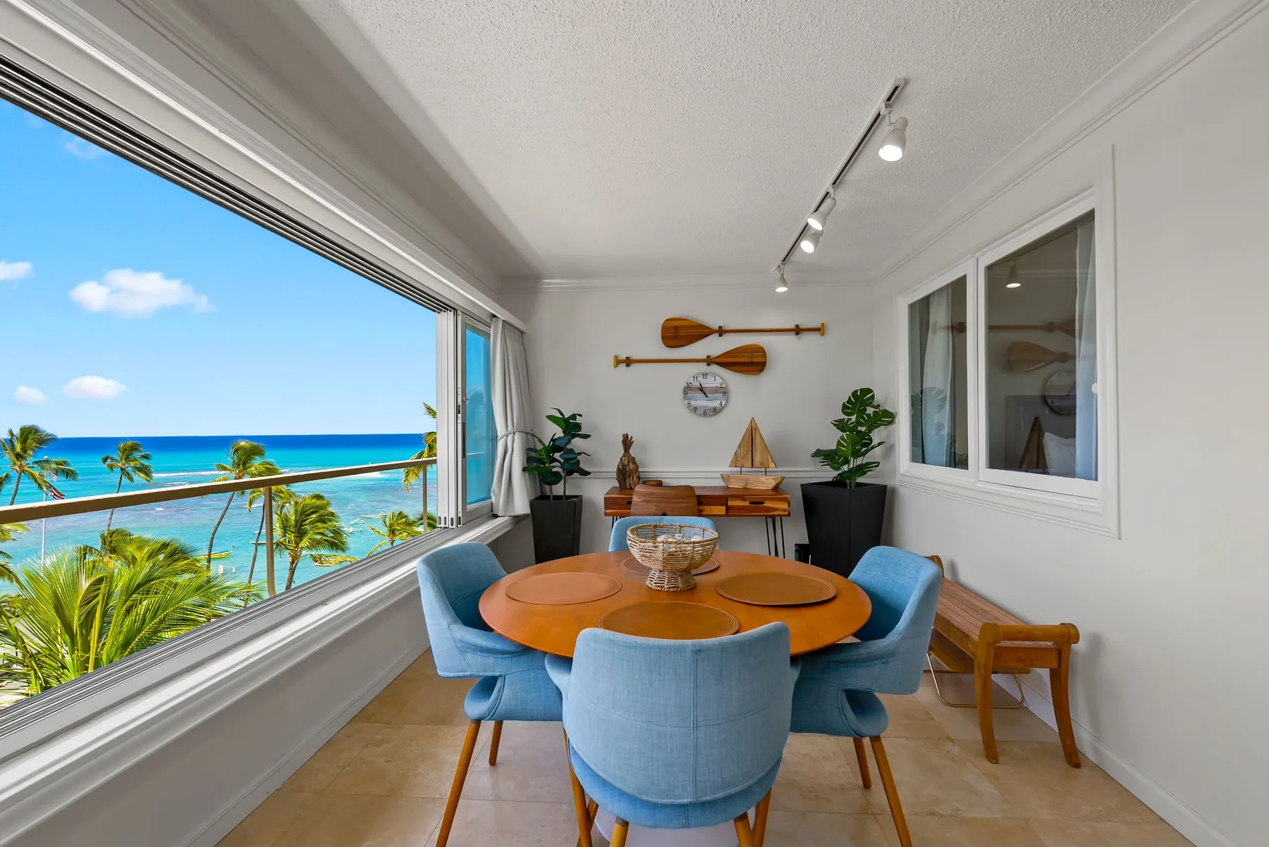 Un comedor luminoso con asientos azules y una amplia ventana con vista al océano.