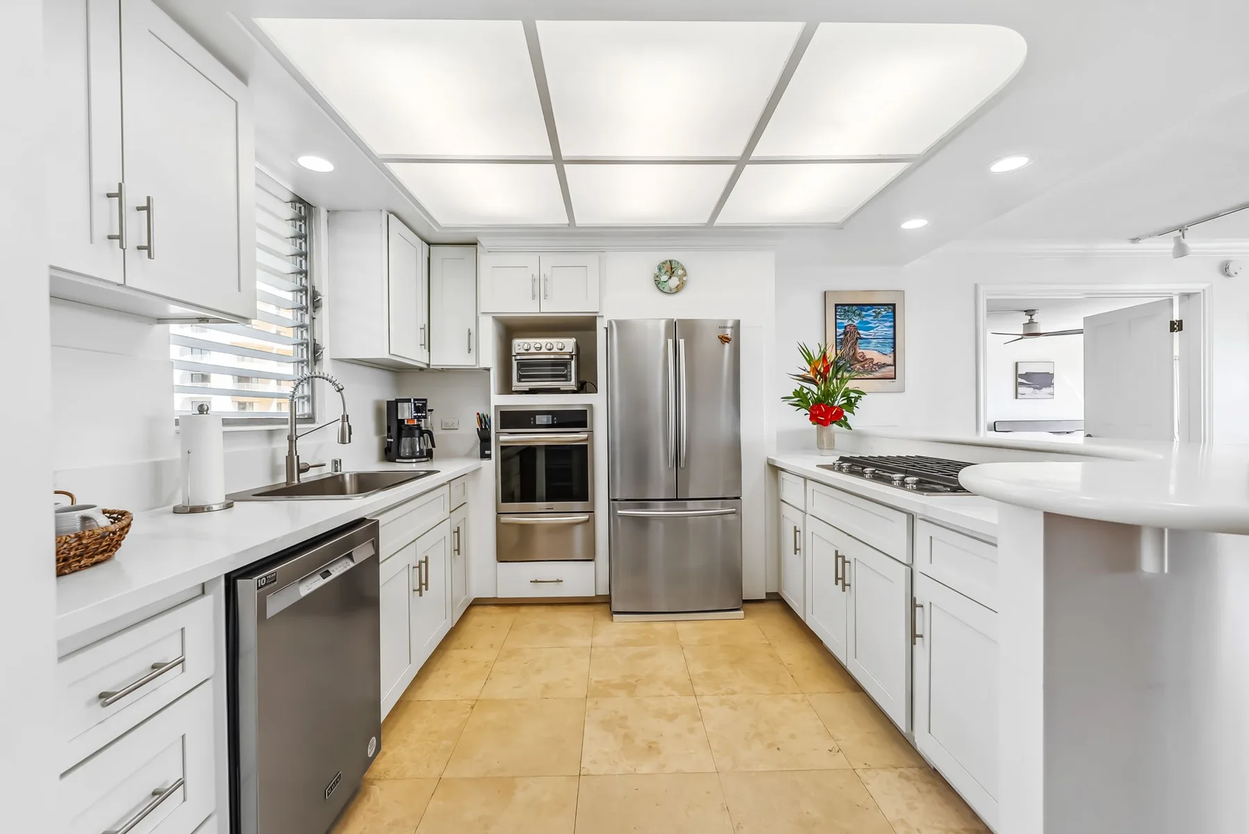 Una cocina blanca y luminosa con electrodomésticos de acero inoxidable y una zona de trabajo central.