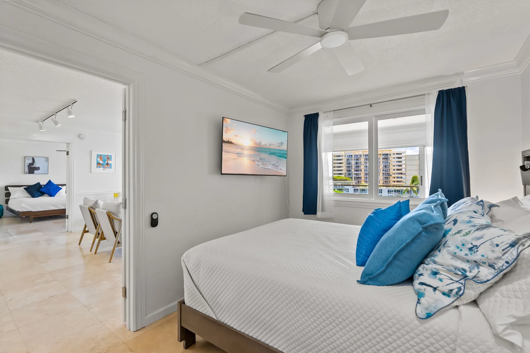 Un dormitorio luminoso con una cama, cojines azules y una ventana con cortinas.