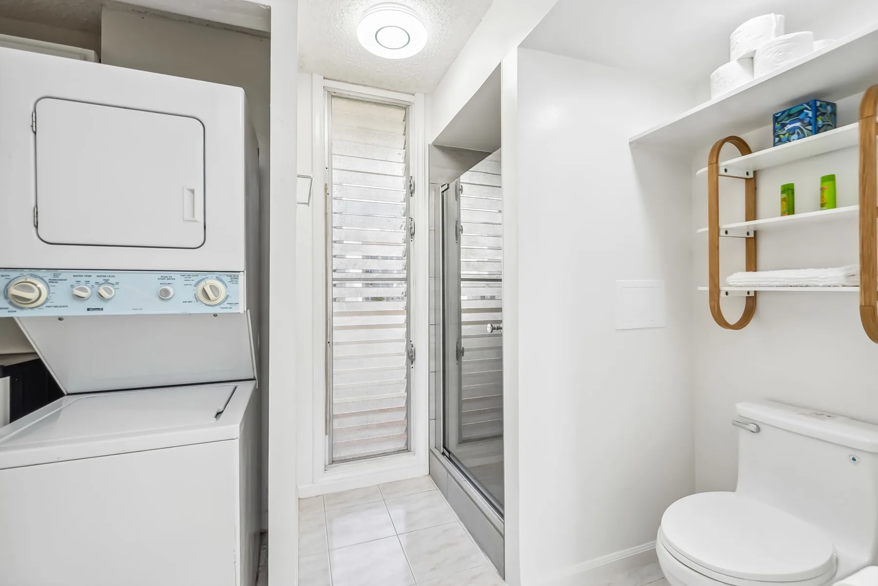 Un baño luminoso con ducha, inodoro y lavadora.