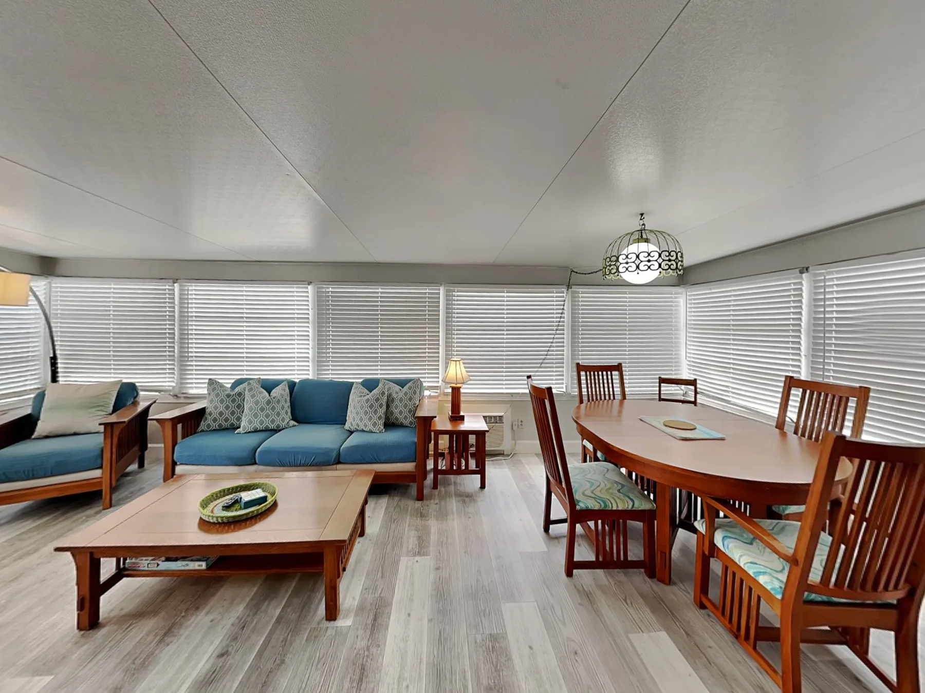 A bright living and dining area has blue seating, a coffee table, and a wooden dining table.