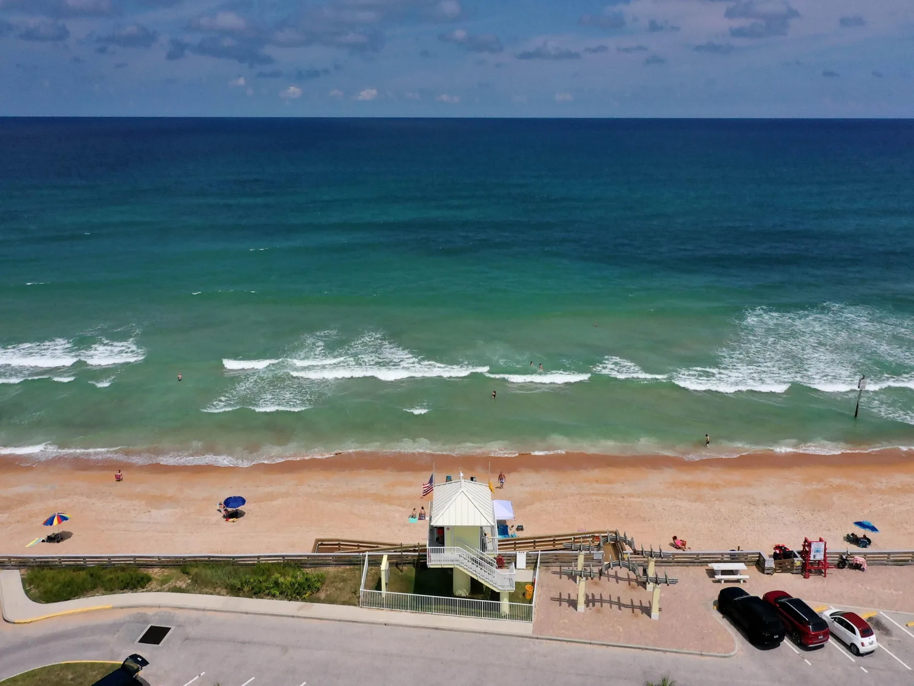 A sandy beach meets turquoise water, with a lifeguard station along the shore.