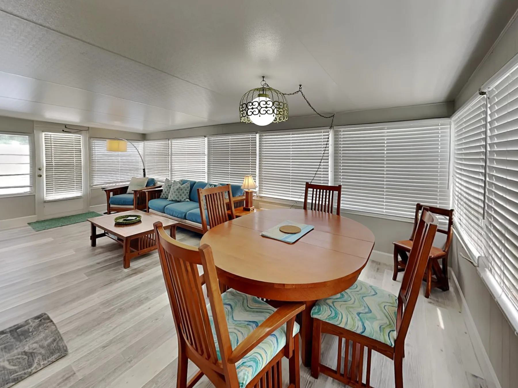 Comedor con mesa y sillas de madera junto a una sala de estar con sofá azul.